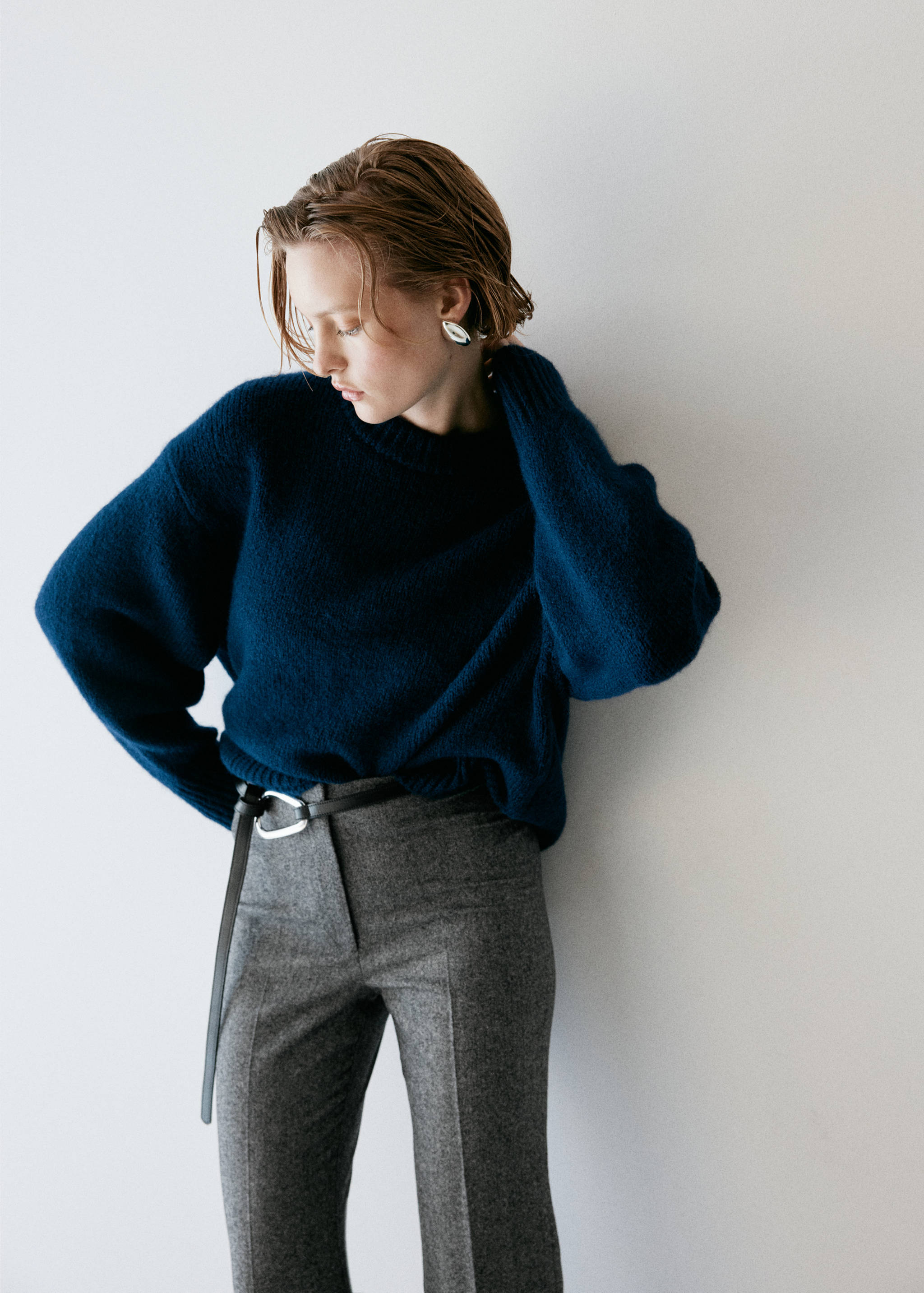 Grey trousers styled with a dark blue knitted jumper and belt.