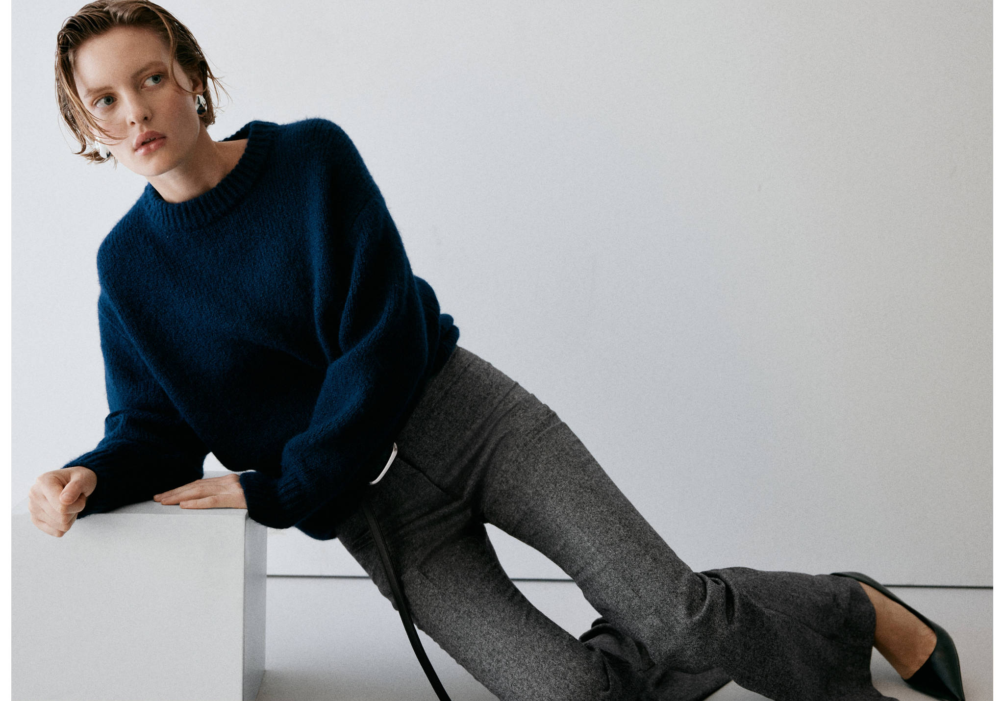 Grey patterned trousers with a flared hem, worn with a dark blue sweater.