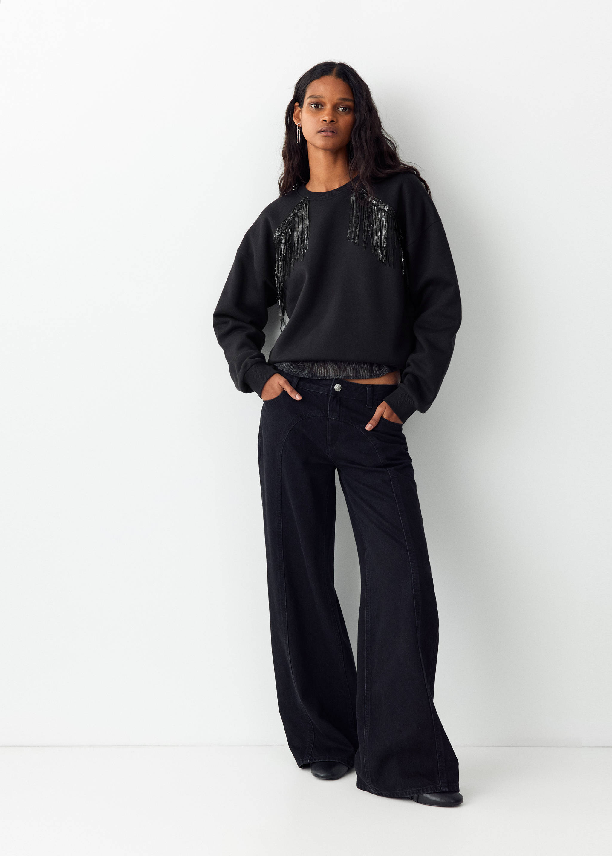 Black sweatshirt with fringed sequin shoulder details and wide-leg trousers.