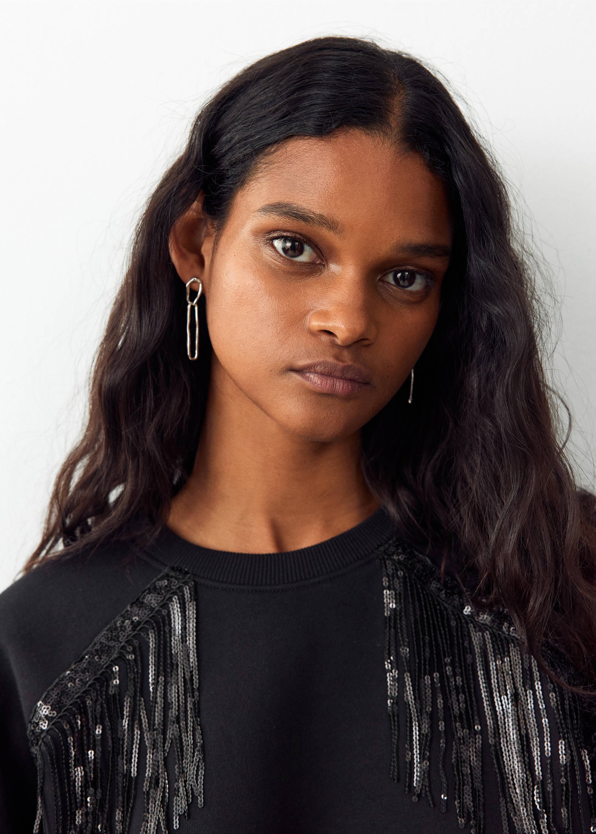 Black sweatshirt featuring sequin fringe shoulder detail in a close-up model view.