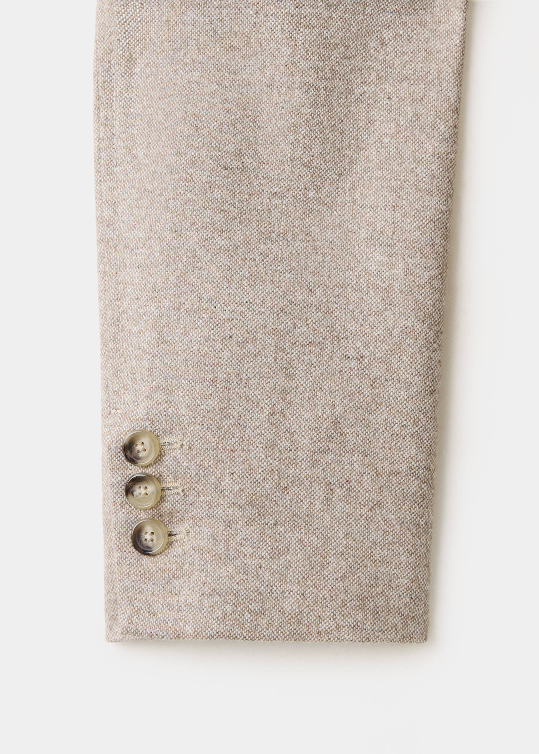 Close-up of a beige textured blazer sleeve with three tortoiseshell buttons.