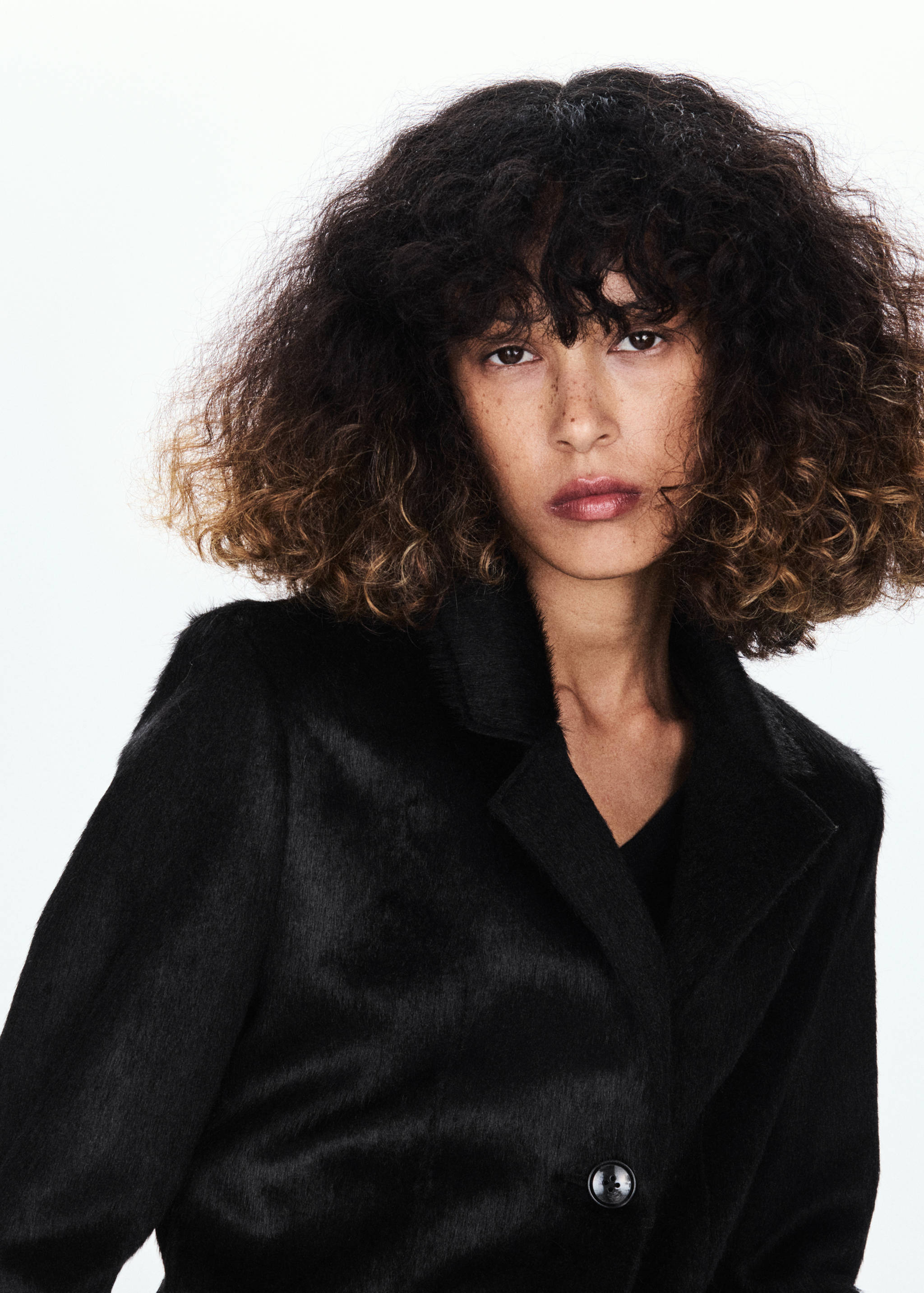 Close-up of a black textured faux-fur coat with a lapel collar.