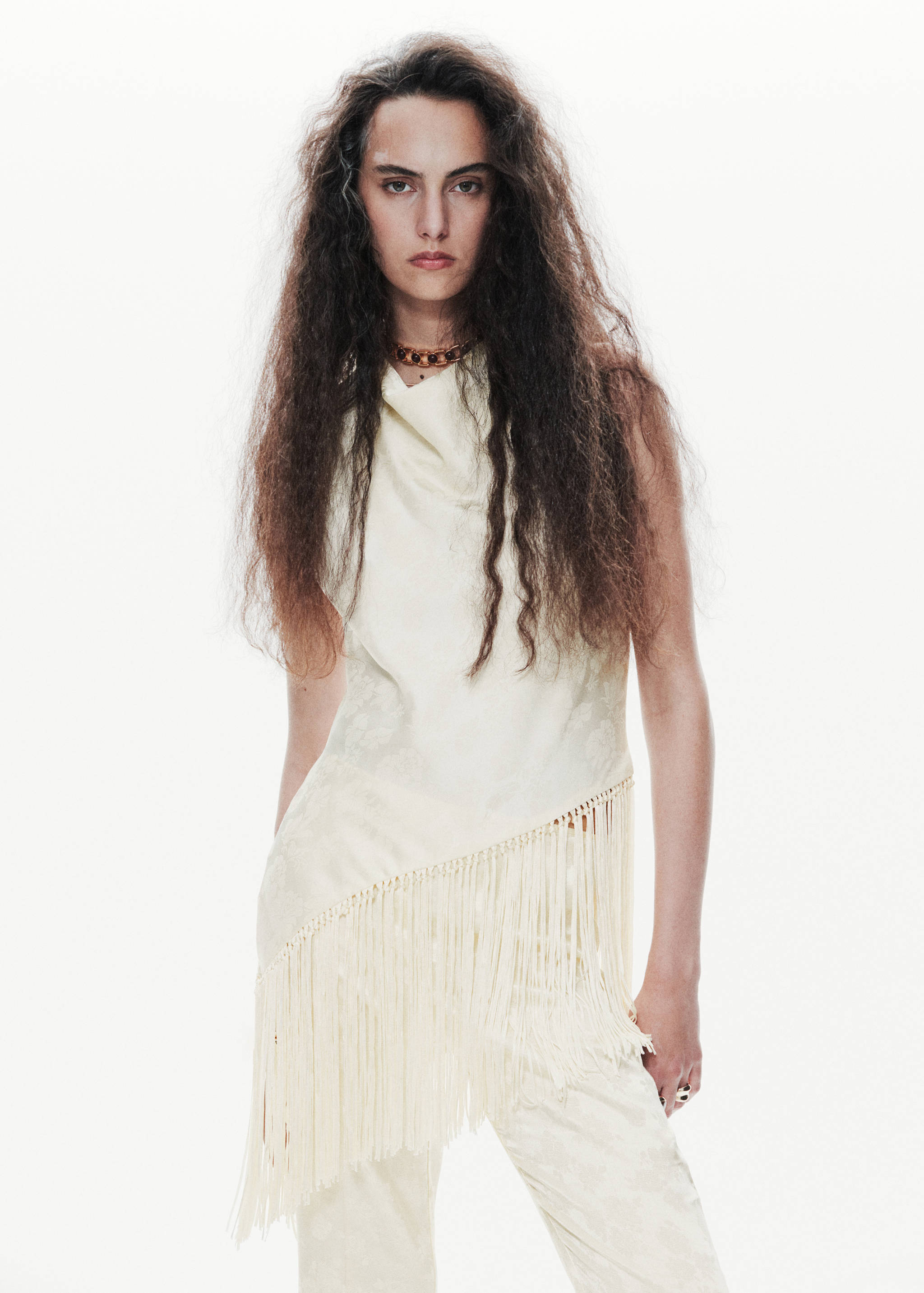Off-white sleeveless top with a cowl neck and asymmetrical fringe hem.