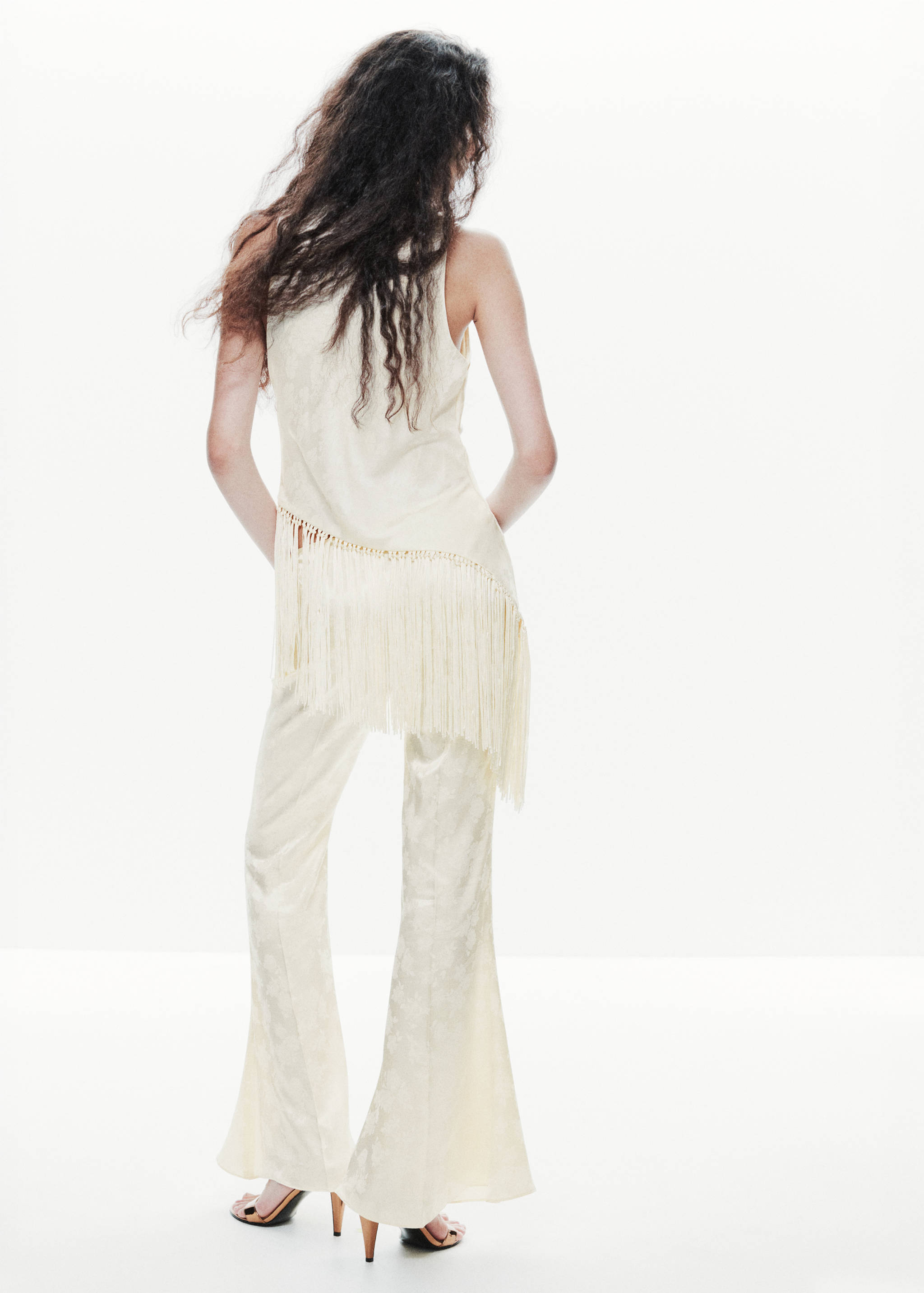 Back view of a sleeveless cream top with an asymmetric fringe hem.