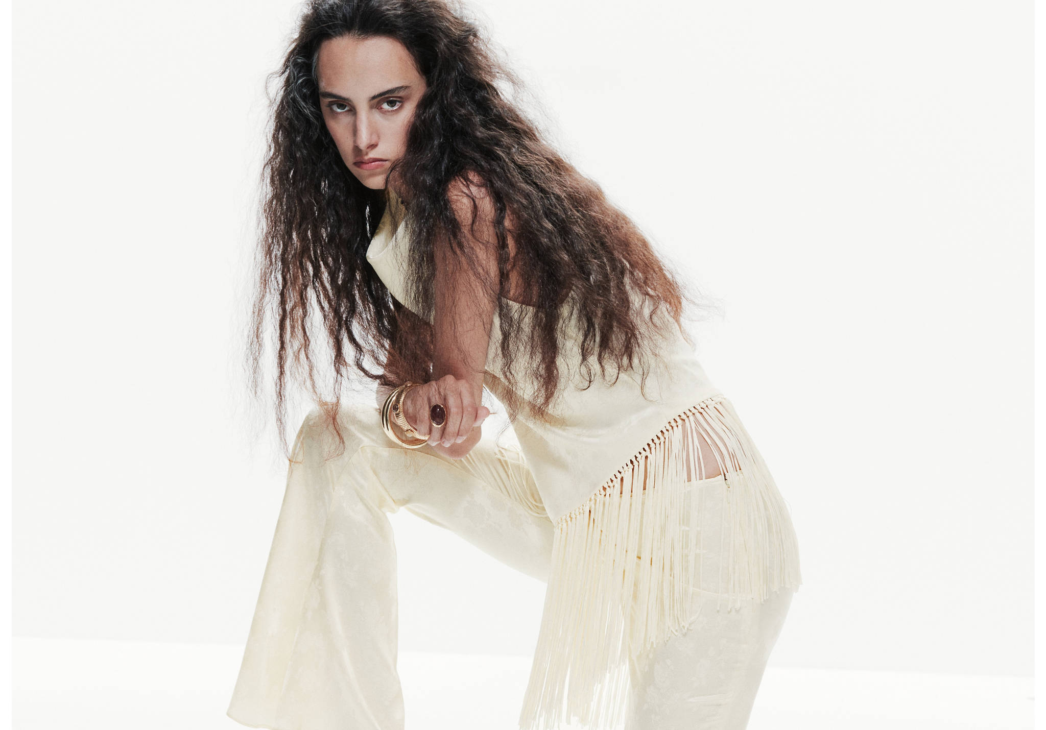 Cream sleeveless top with a high neck and long fringed hem.