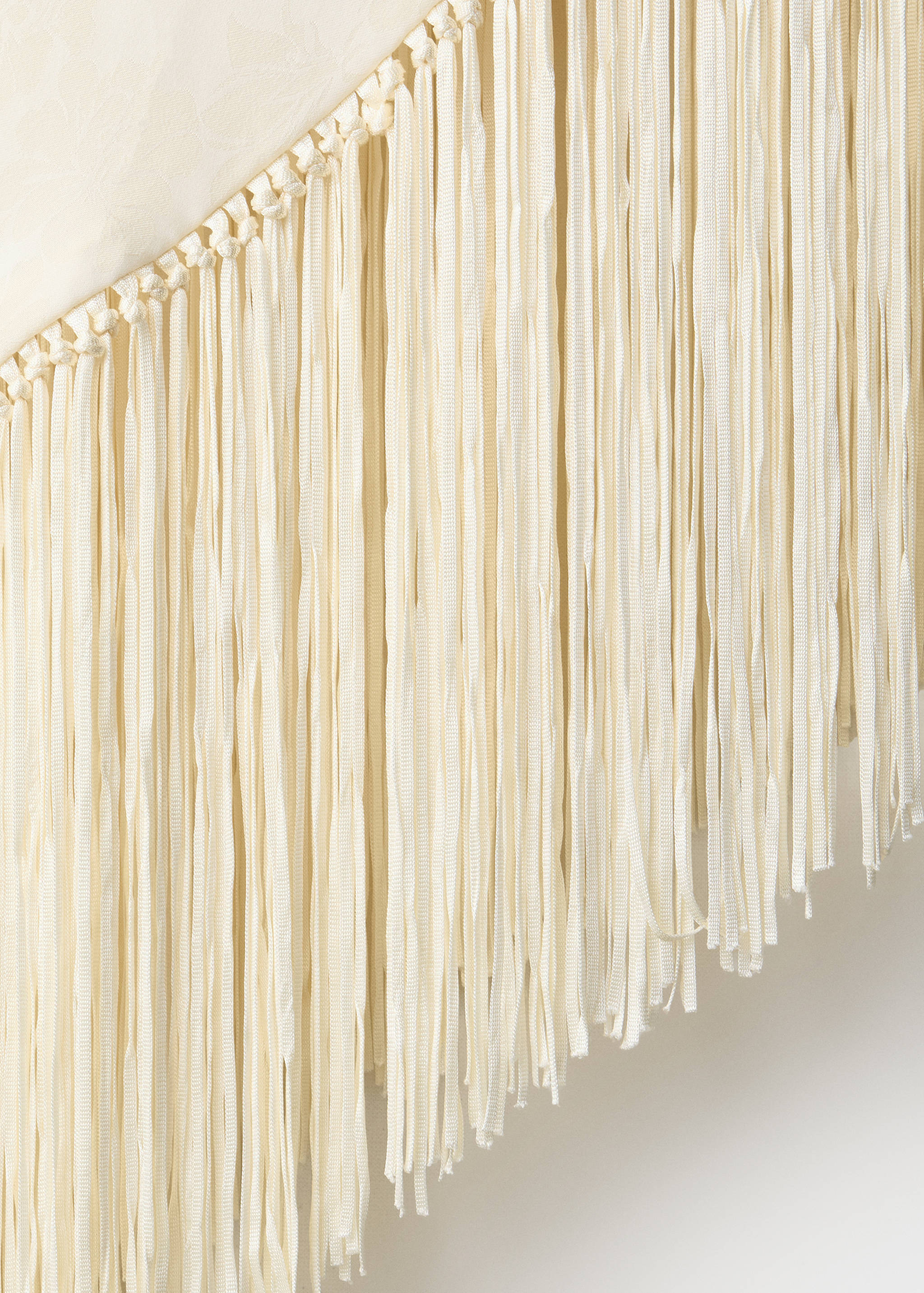 Off-white top detail with long hanging fringe and knotted trim.