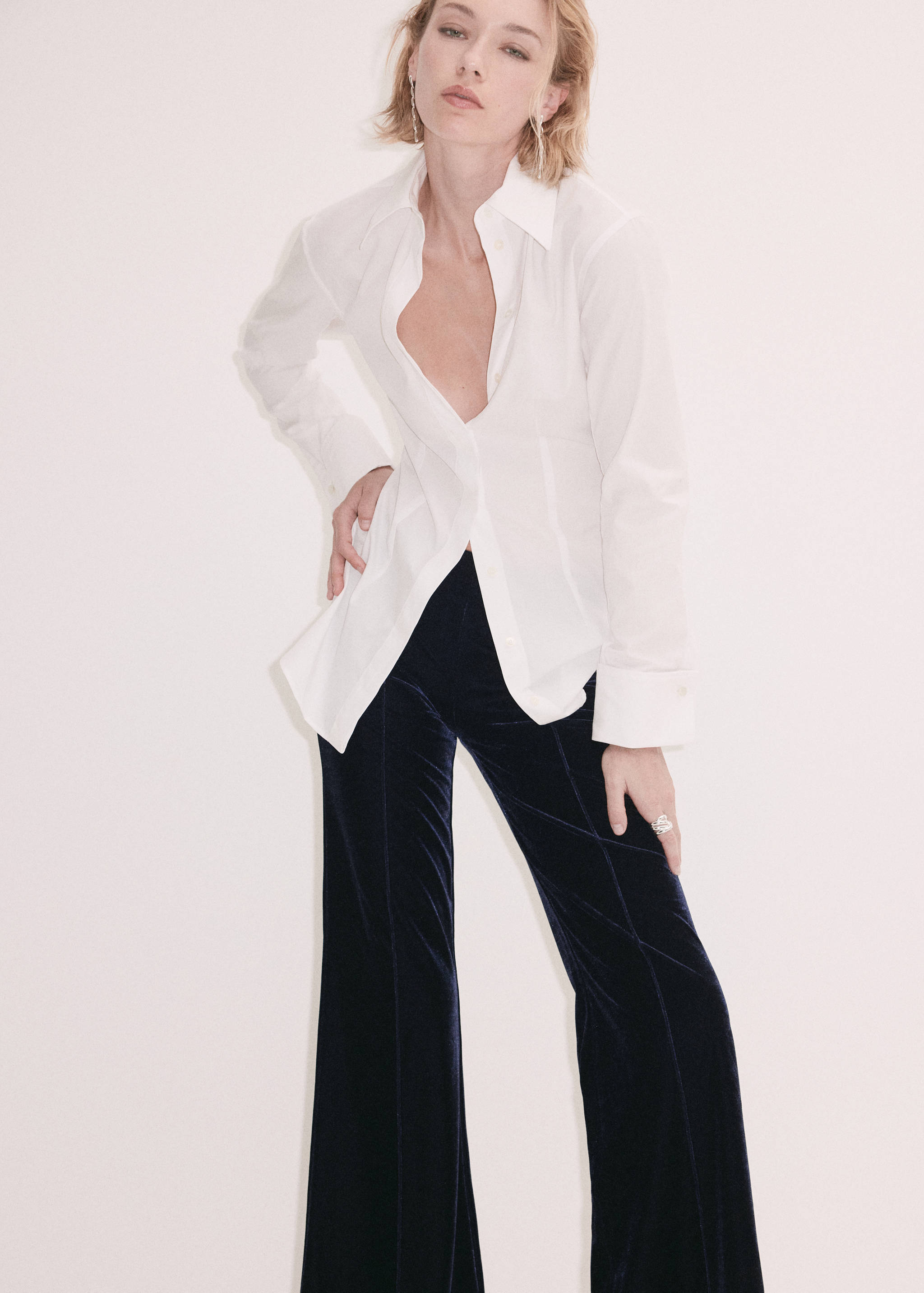 Pantalones oscuros de terciopelo combinados con una camisa blanca abotonada.