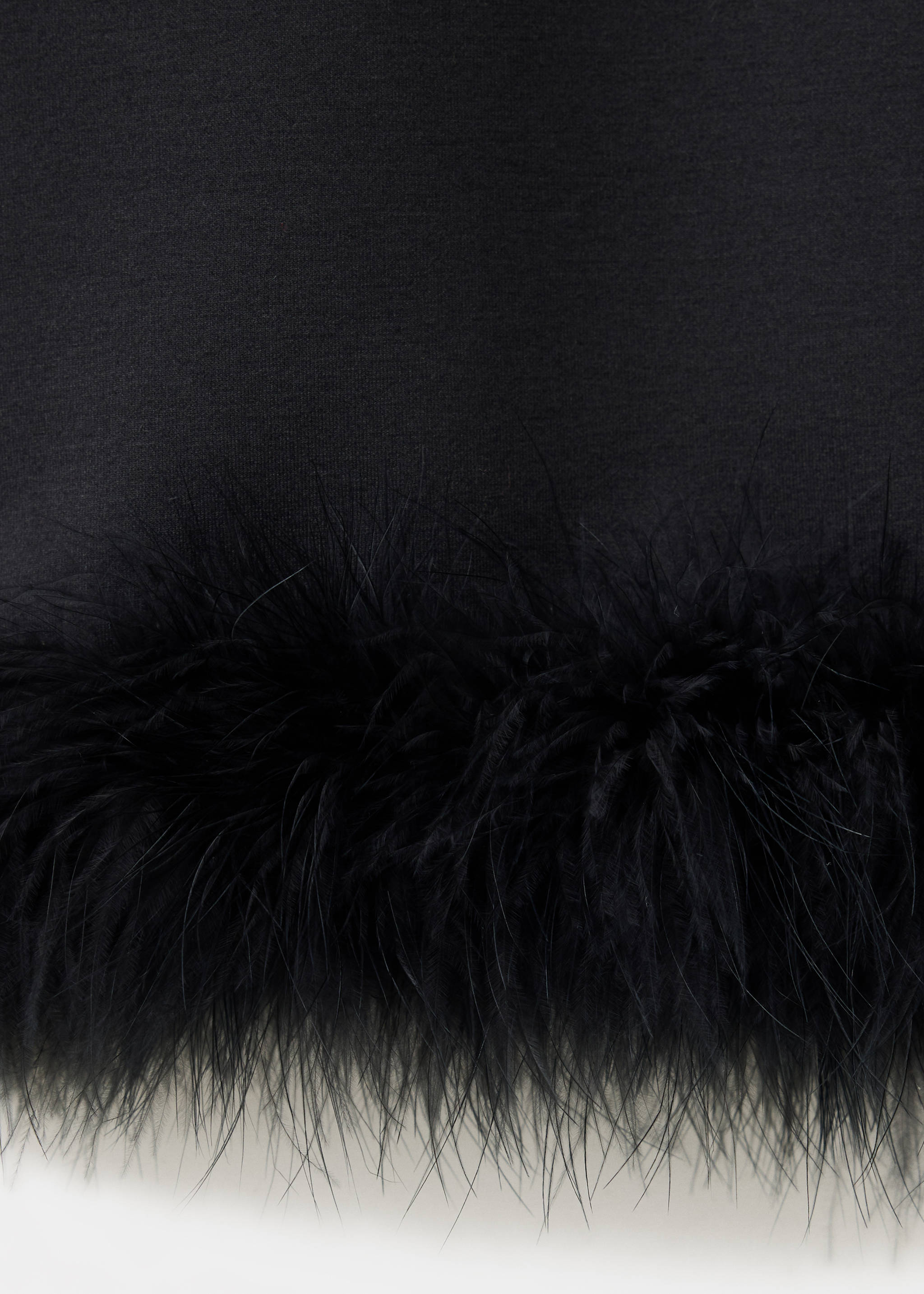 Close-up of black trousers with faux-feather hem trim.