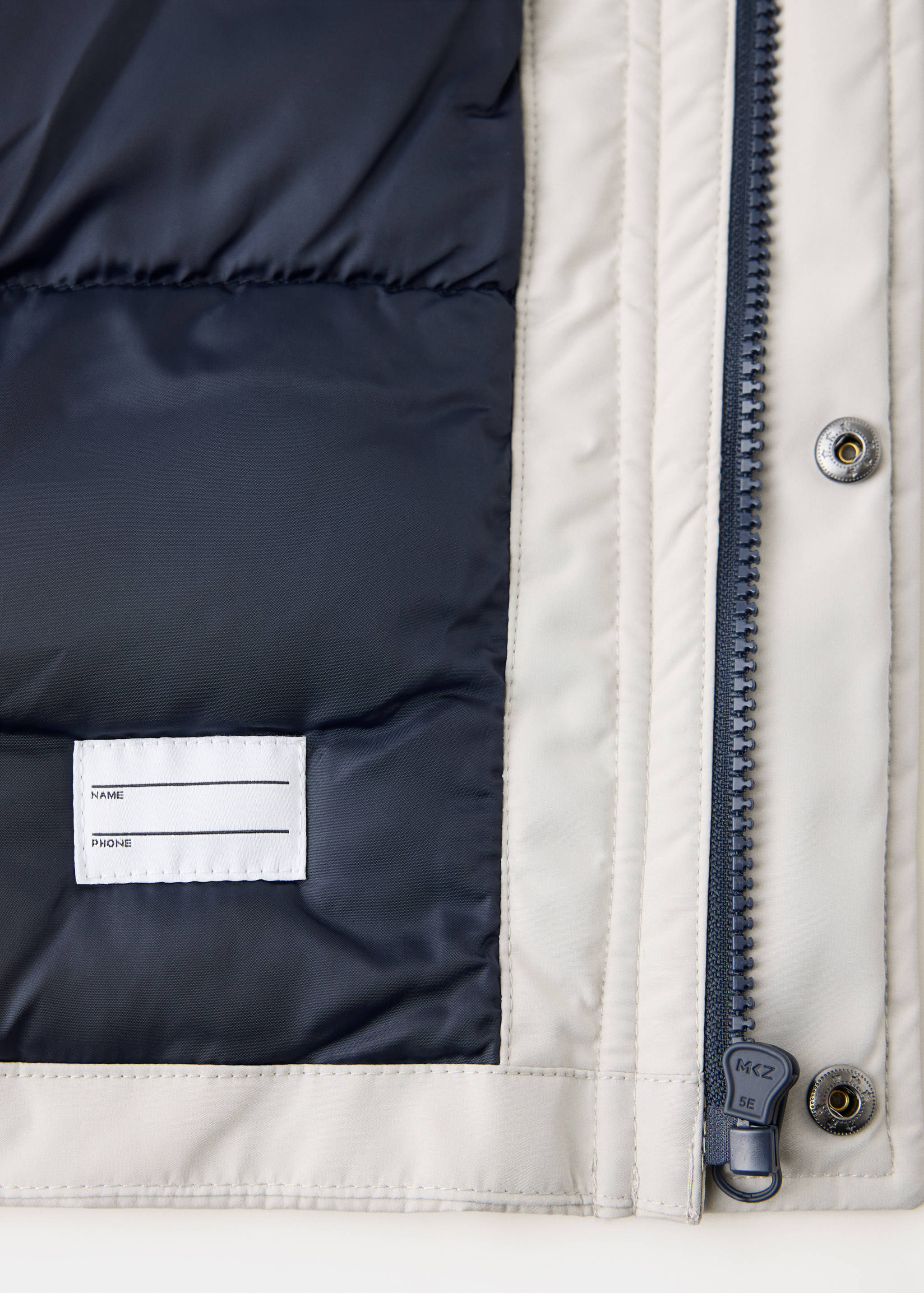 Close-up of off-white kids' anorak fabric, navy lining, and zipper detail