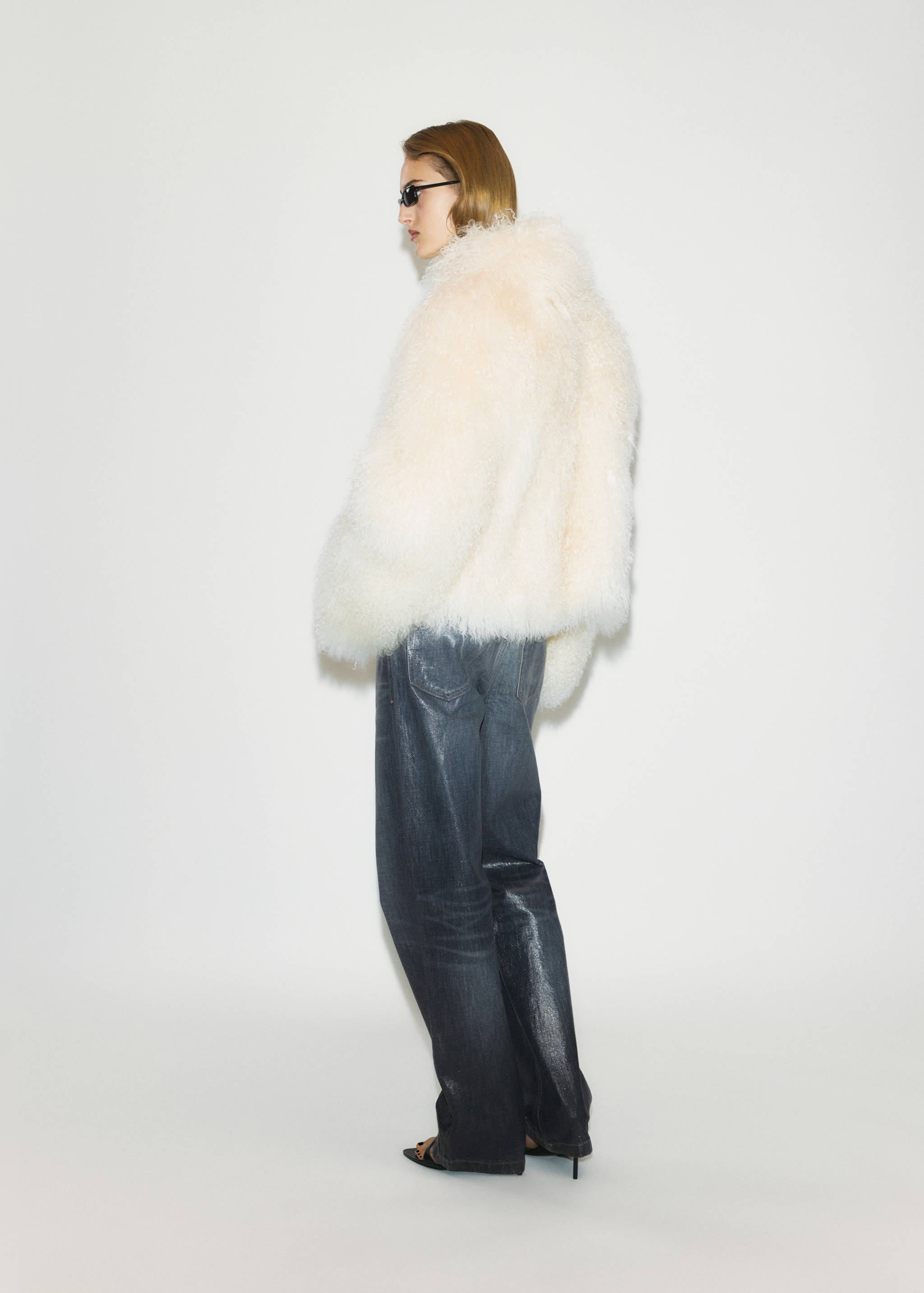 Back view of dark grey denim trousers worn with a voluminous off-white faux-shearling jacket.