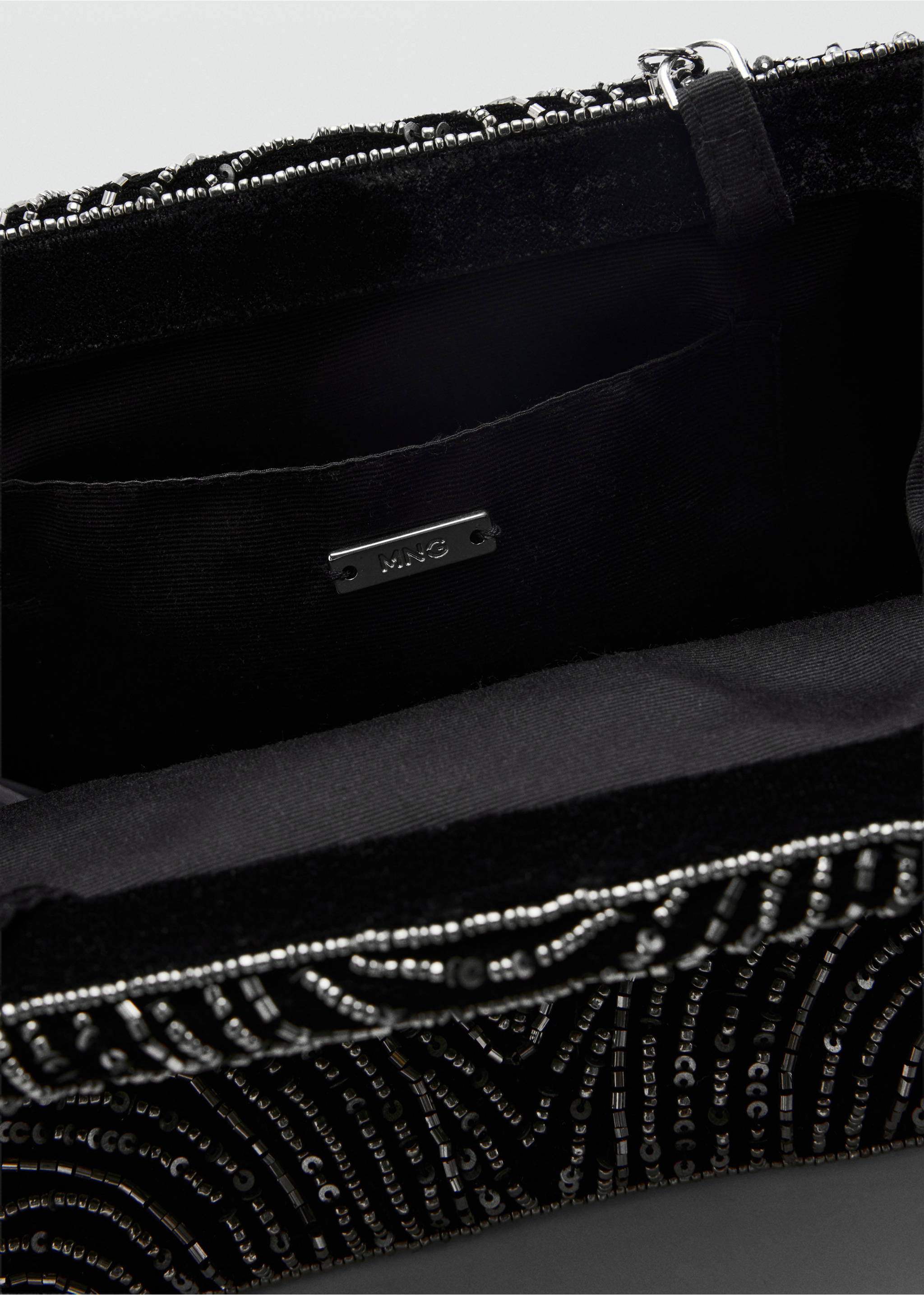 Close-up of a black handbag interior showing the brand plaque and beaded exterior., Black. Ref: 37079209-00.