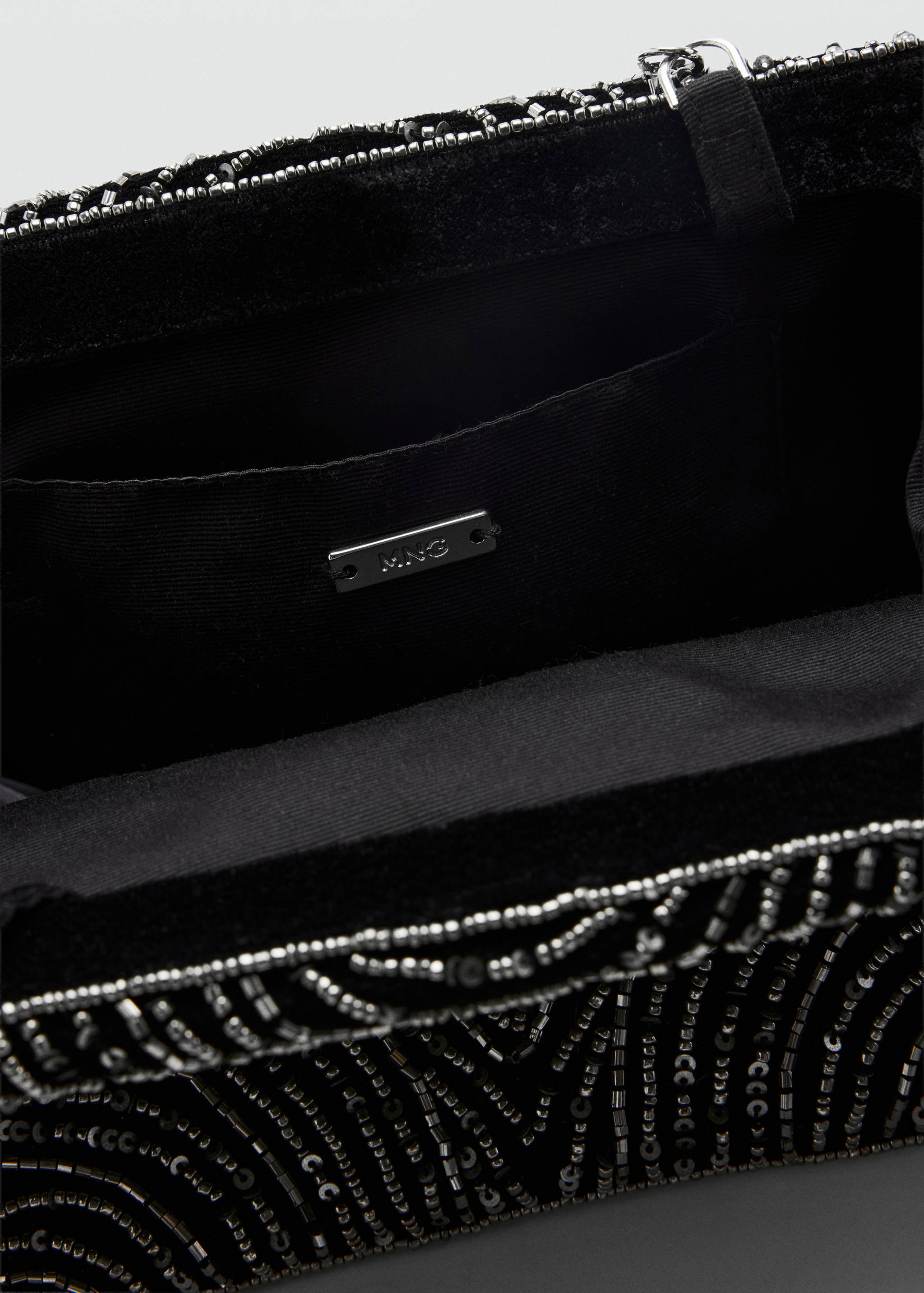 Close-up of a black handbag interior showing the brand plaque and beaded exterior.