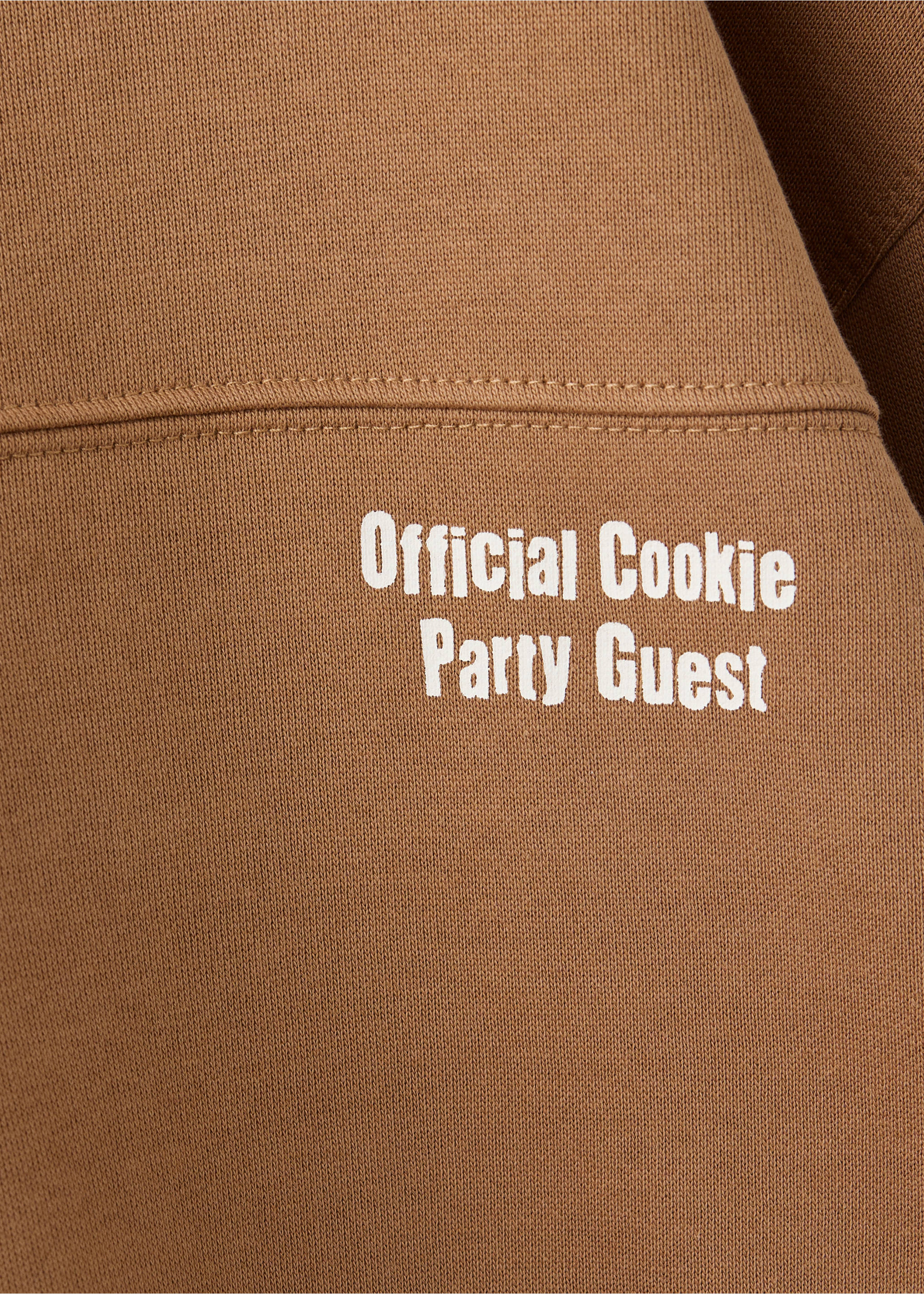 Brown sweatshirt close-up with white Official Cookie Party Guest text., Caramel. Ref: 37079213-00.