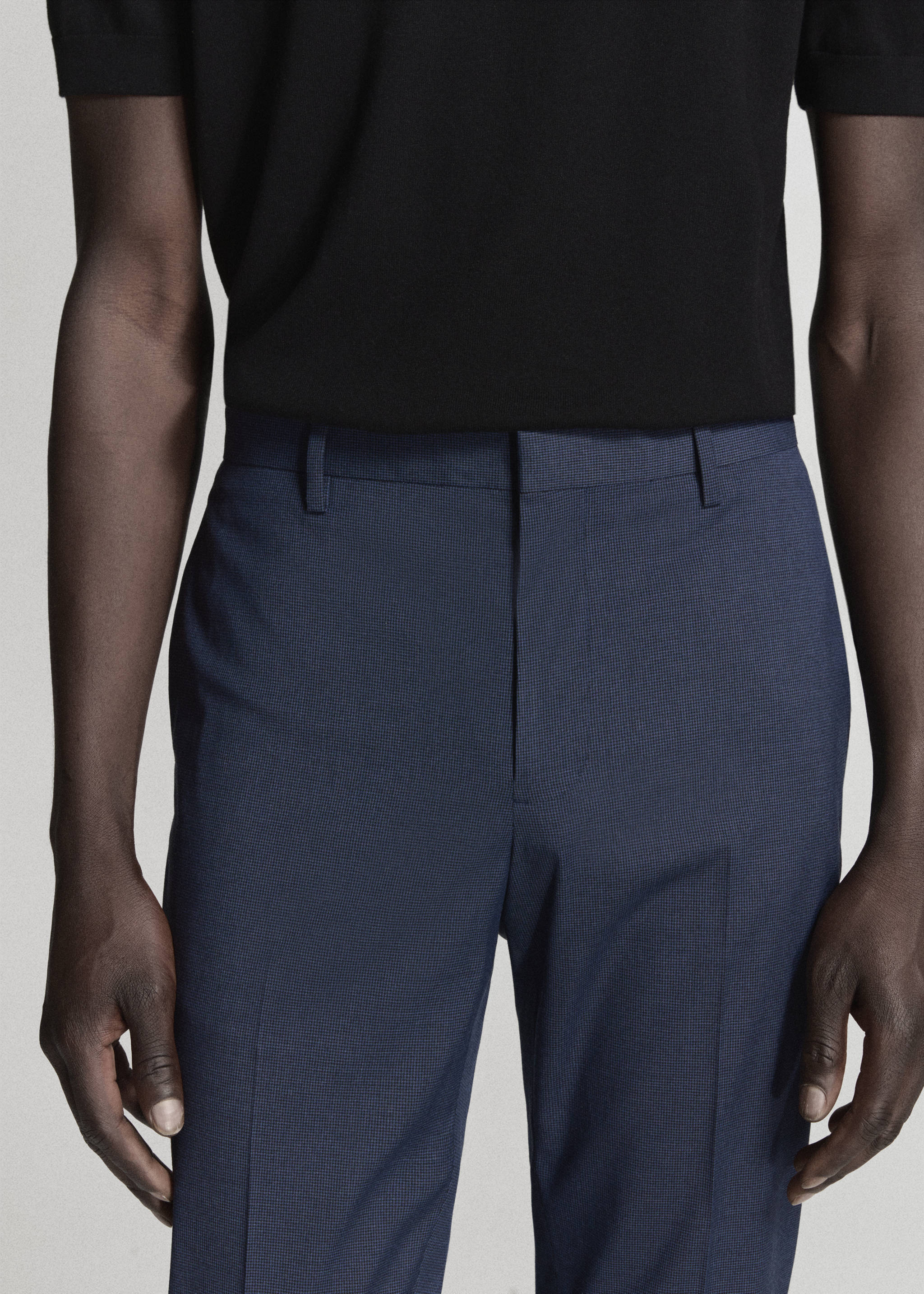 Close-up of blue tailored trousers with belt loops, worn with a black polo.