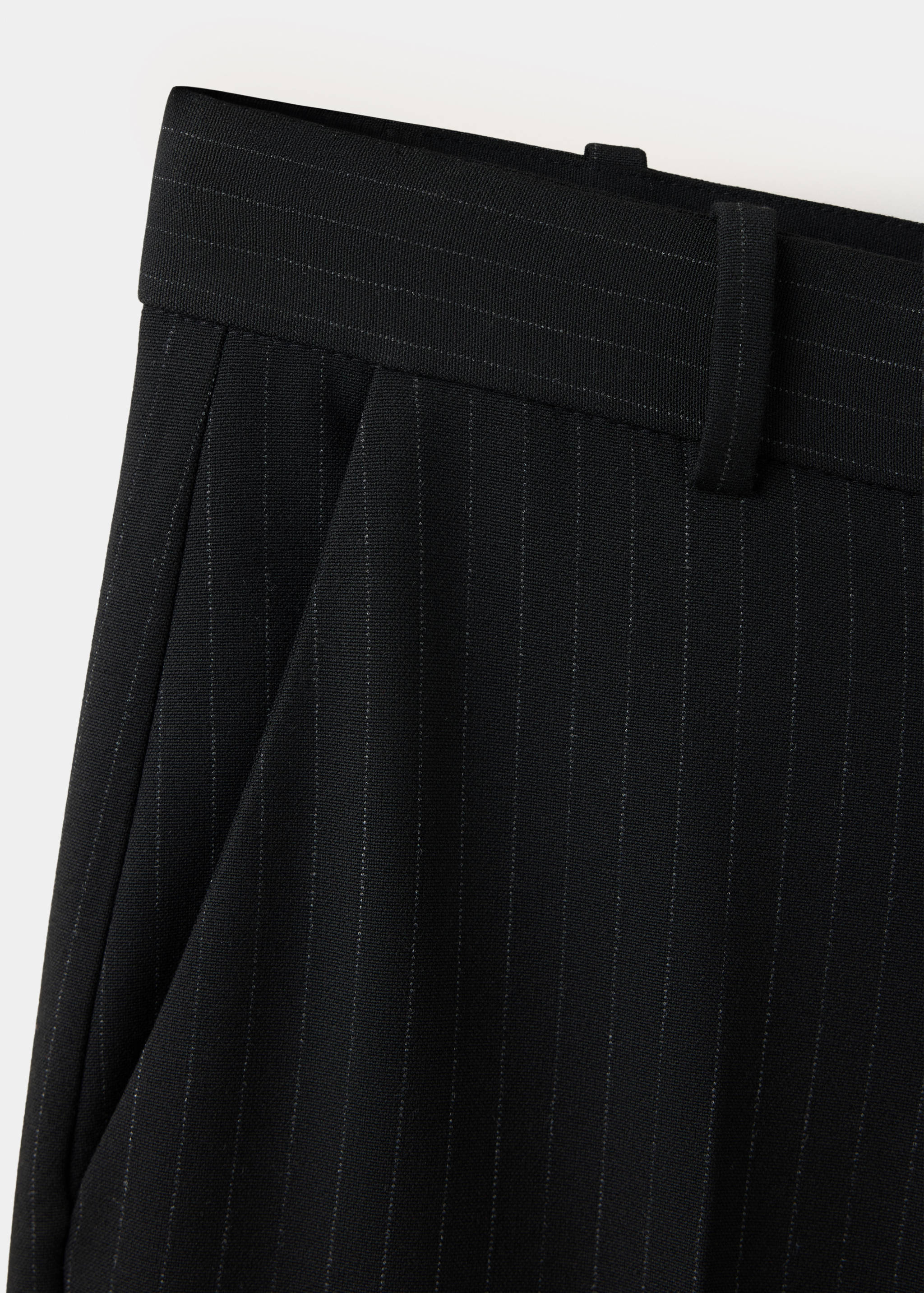 Detalle de pantalón negro de raya diplomática con pretina estructurada y pinzas.