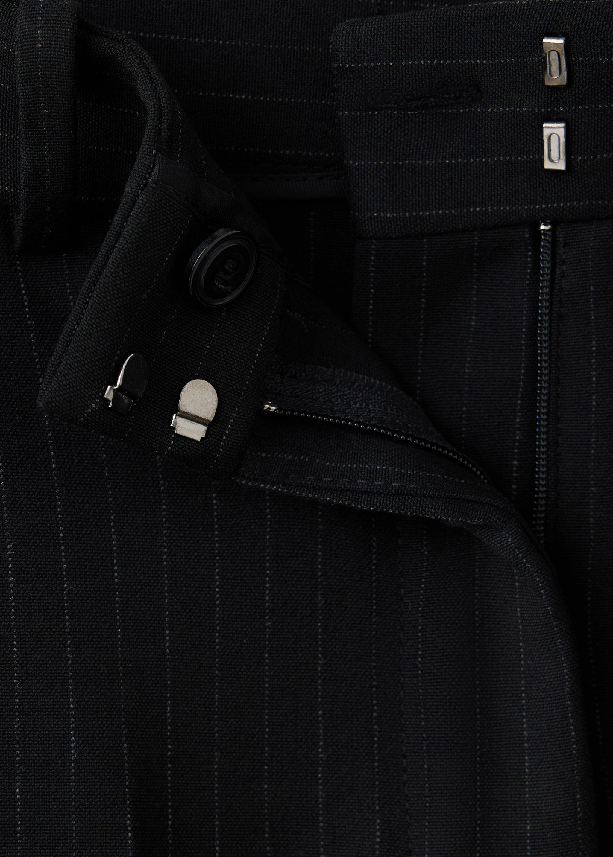 Detalle del pantalón negro de raya diplomática, con enfoque en la cinturilla y los detalles de cierre.