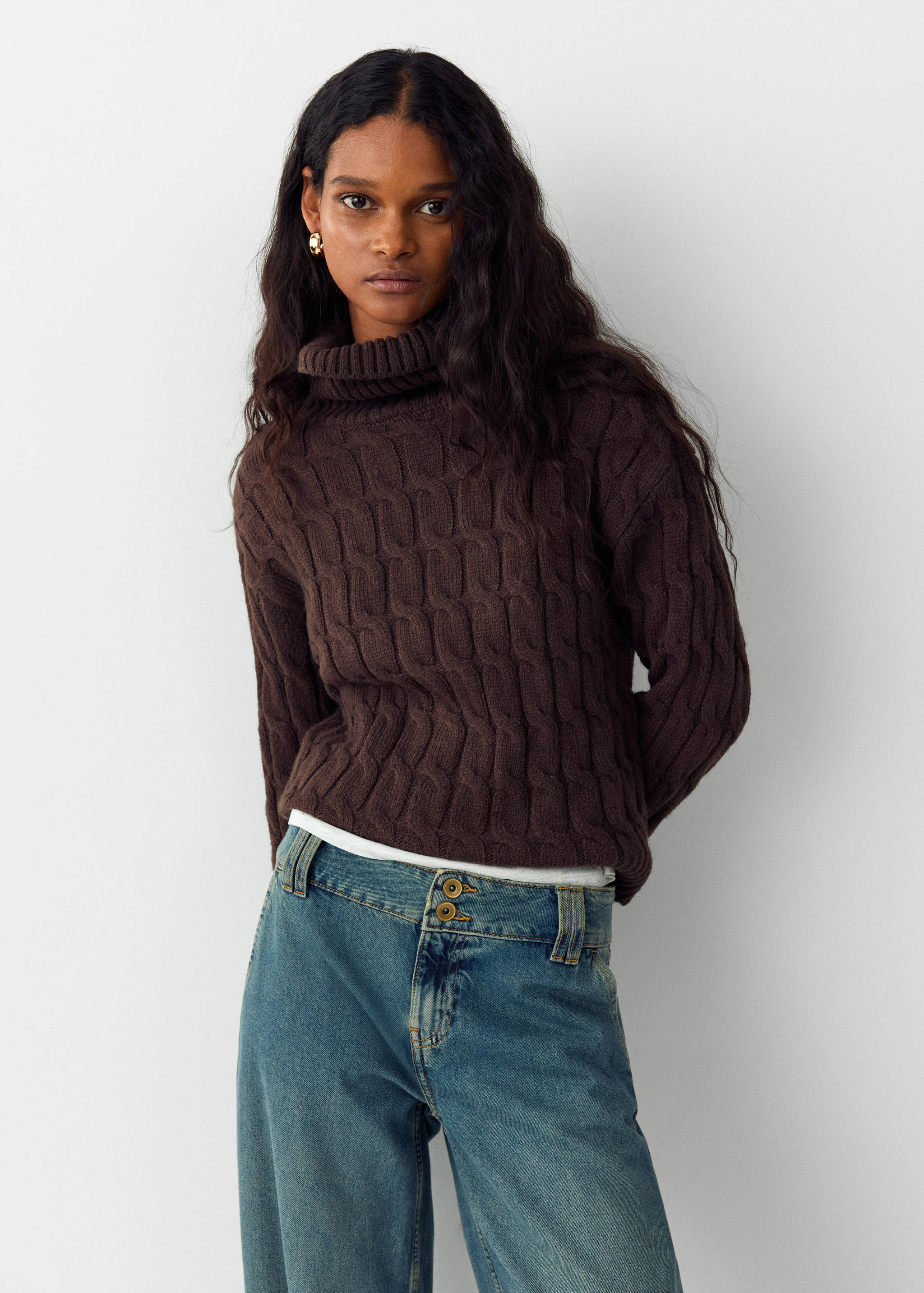 Dark brown cable-knit turtleneck sweater worn with blue denim trousers.