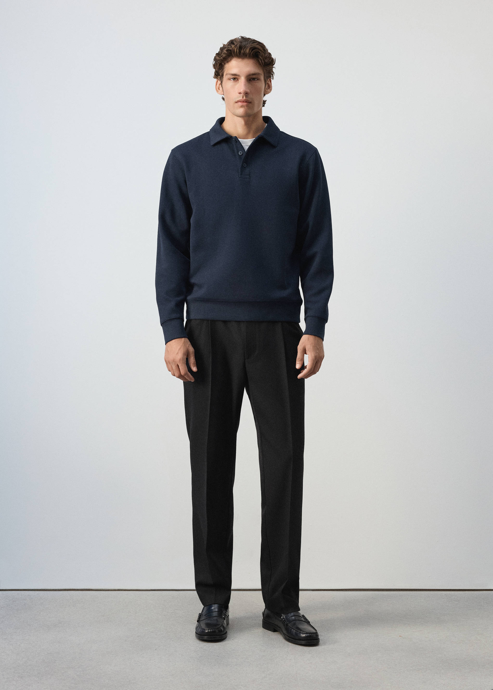 Dark blue polo sweatshirt with a button placket, worn with black trousers.