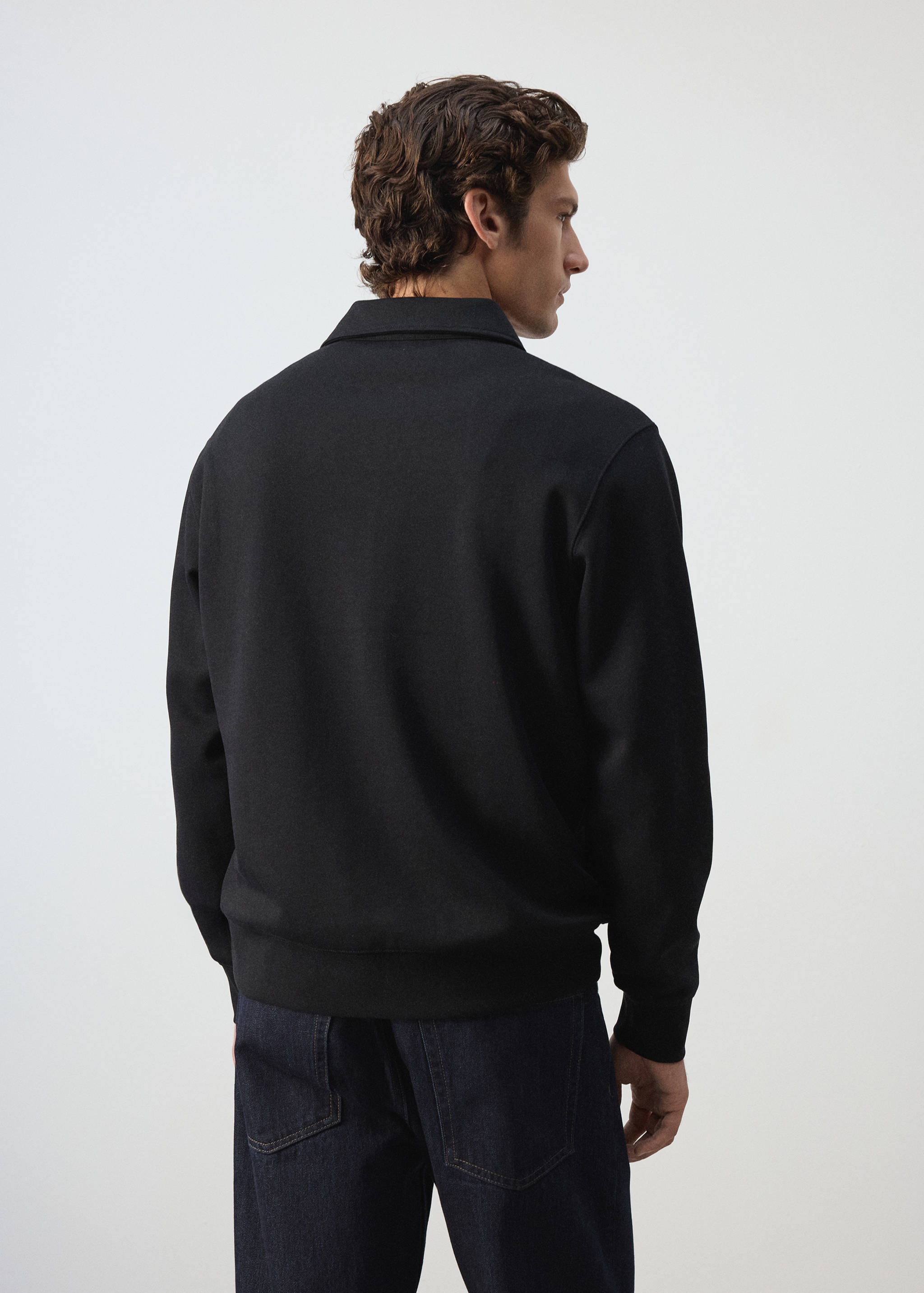 Back view of a black sweatshirt with a collar, worn by a male model.