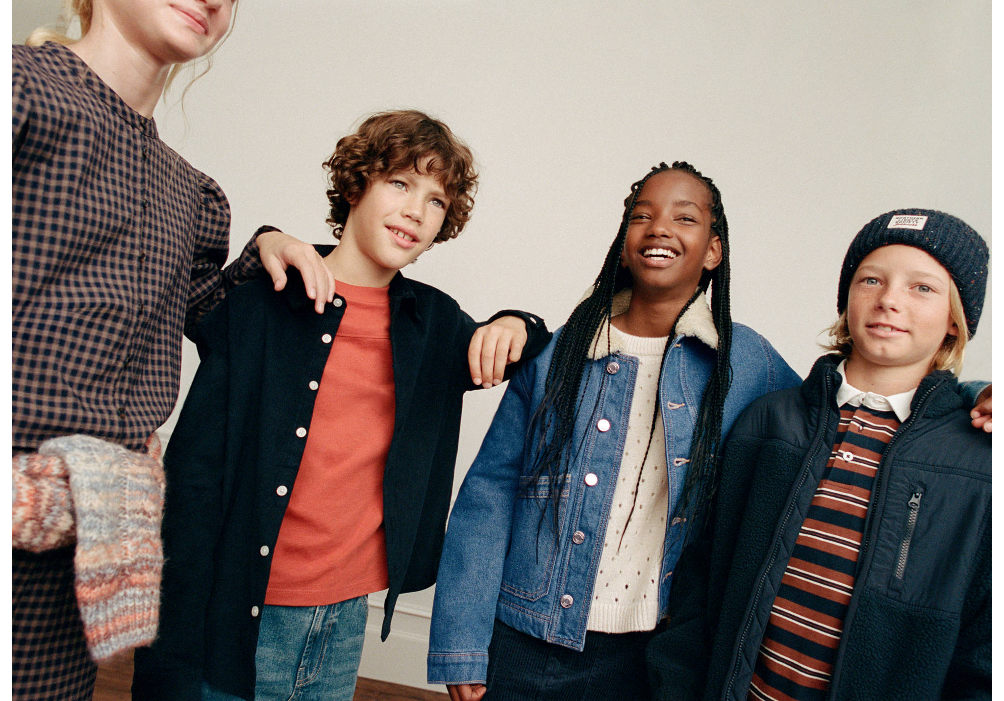 Four child models wearing casual shirts, jackets, and knitwear in a studio.