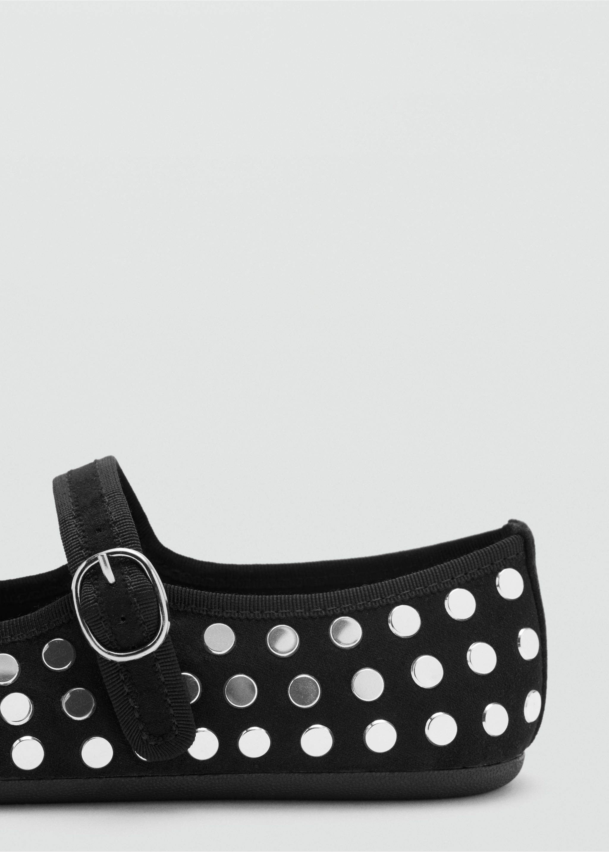 Close-up of a black flat shoe with silver grommets and a buckled strap., Black. Ref: 37086360-00.