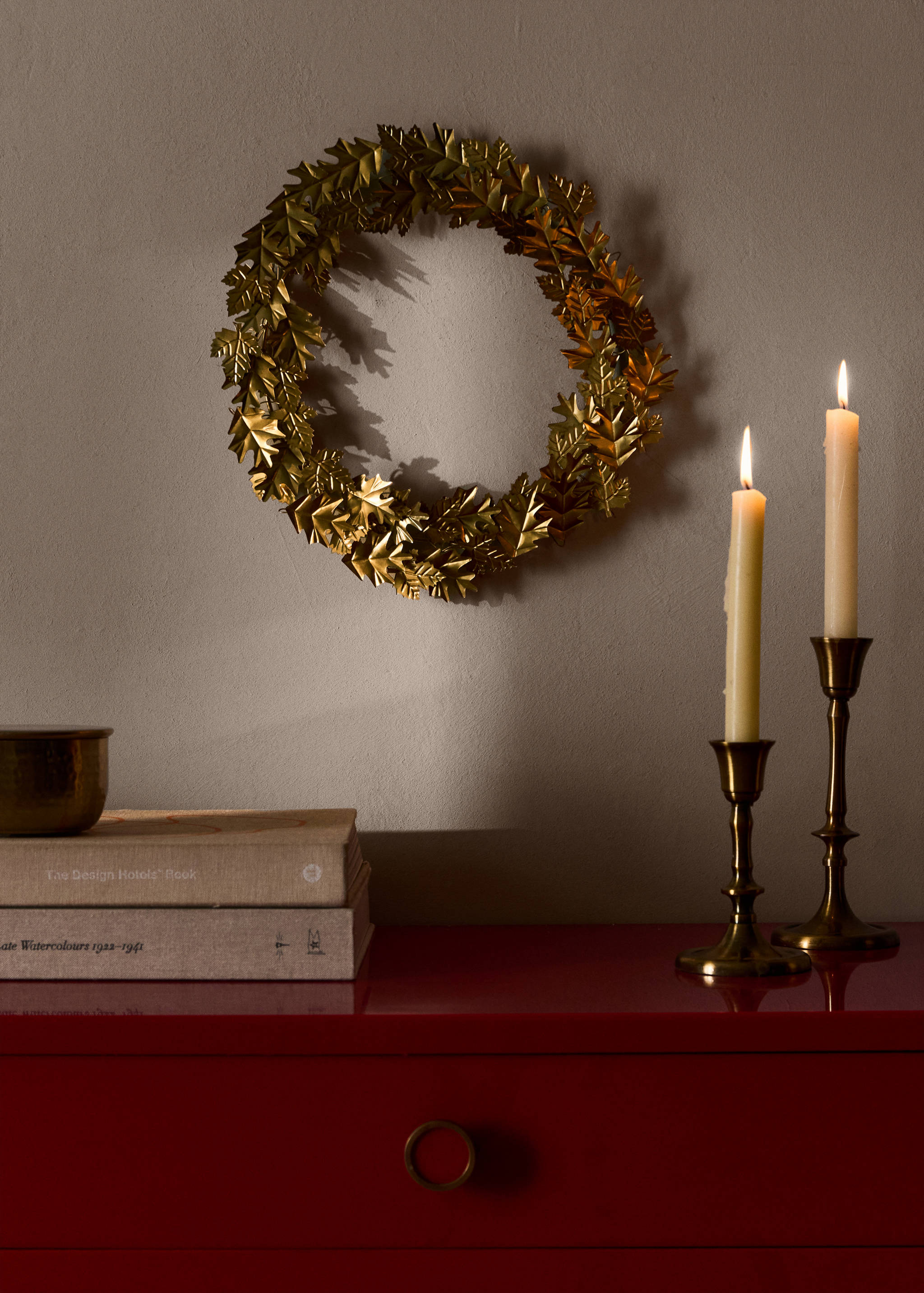 Decorative gold leaf wreath hanging on a wall above lit candles.