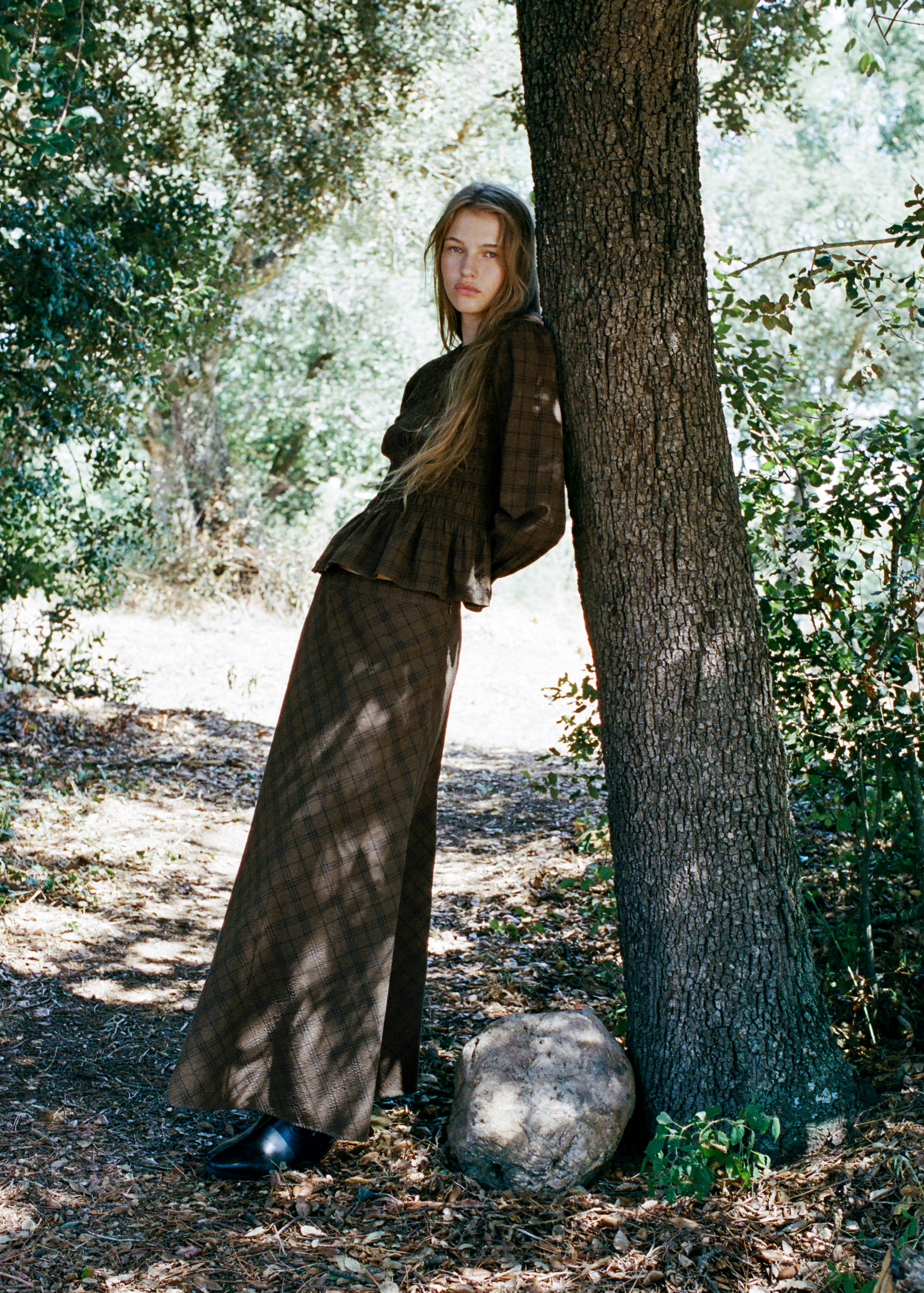 Brown plaid skirt with a matching long-sleeved peplum top in a wooded setting.