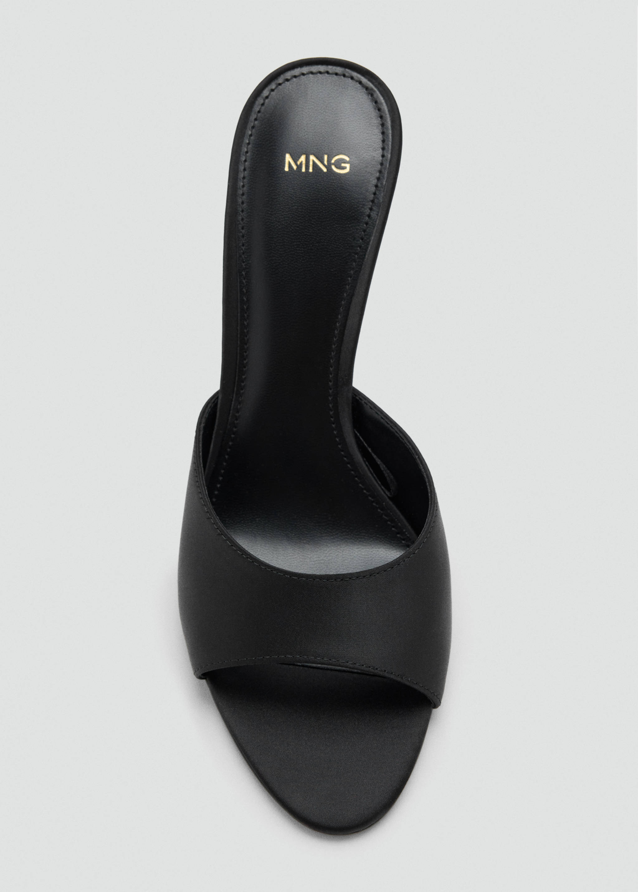 Close-up of a black heeled sandal with an open toe and gold logo detail.