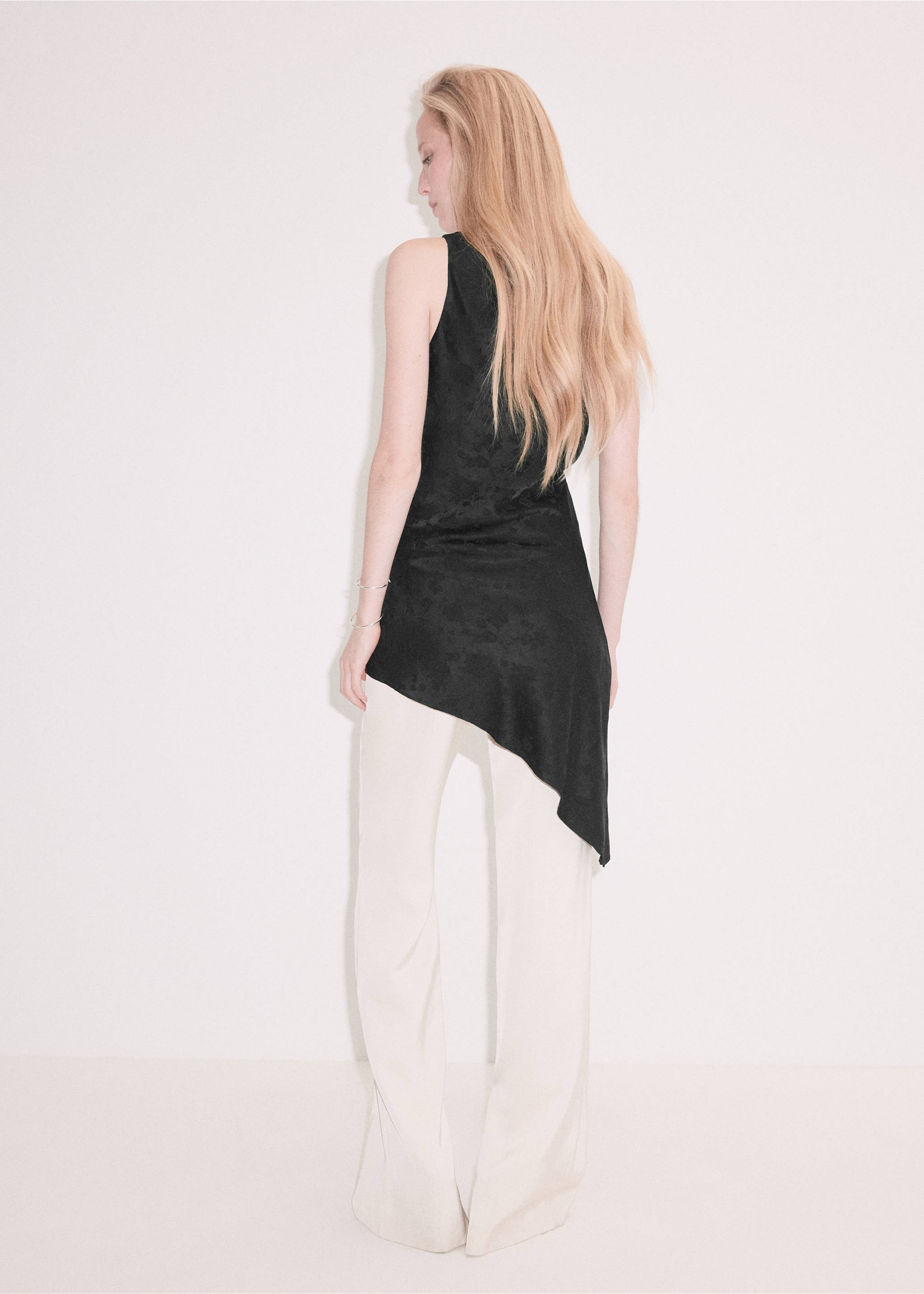 Back view of a black sleeveless asymmetric top worn with light trousers, Black. Ref: 37087783-00.