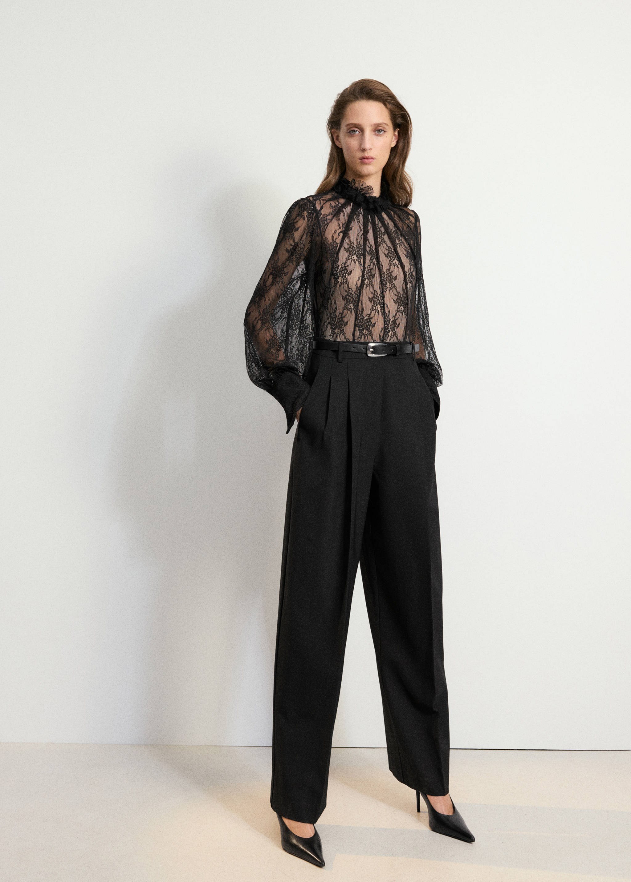 Top negro de encaje transparente con cuello alto con volantes y mangas largas abullonadas.