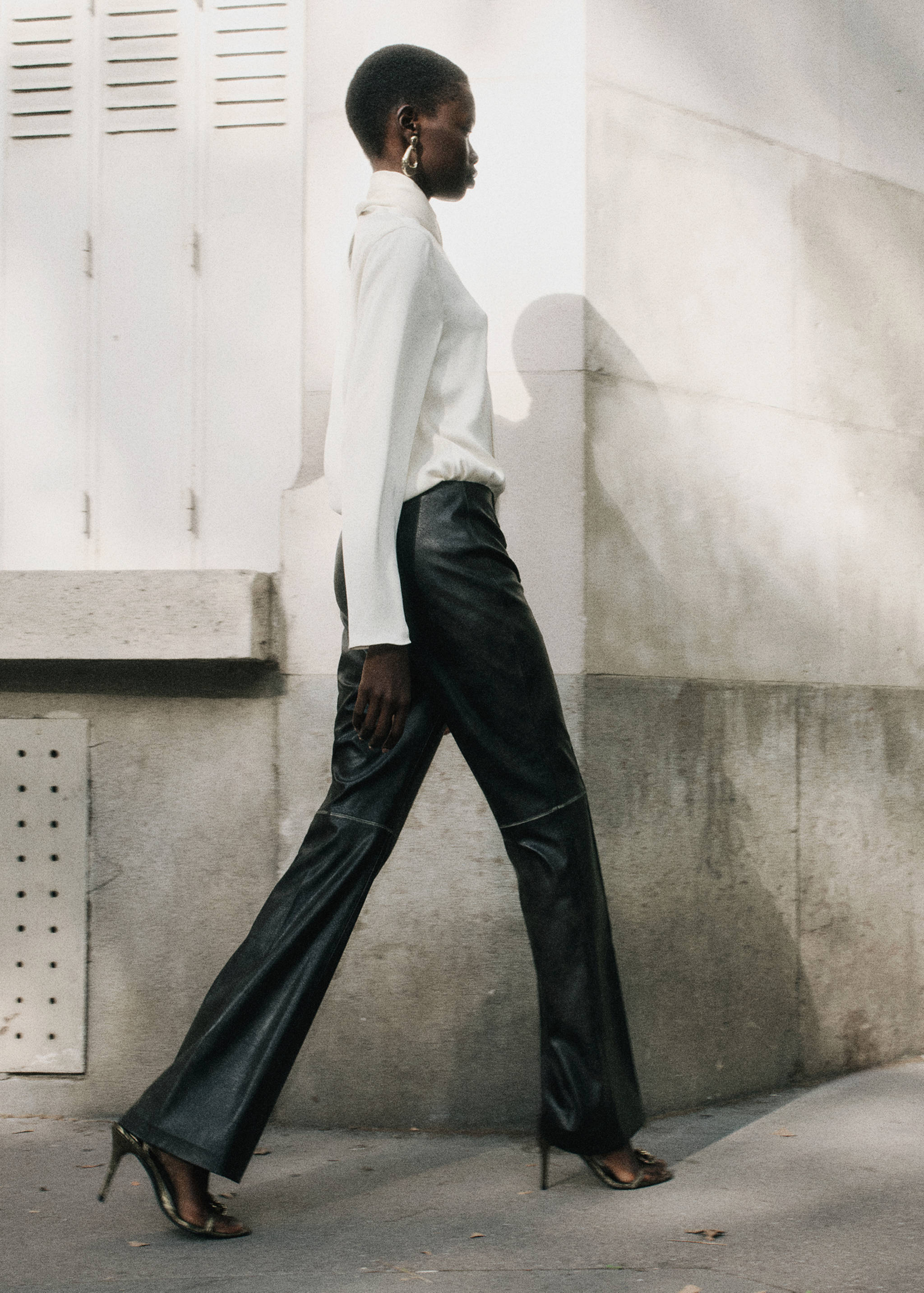 Black straight-leg trousers with horizontal knee seams, paired with a white blouse.