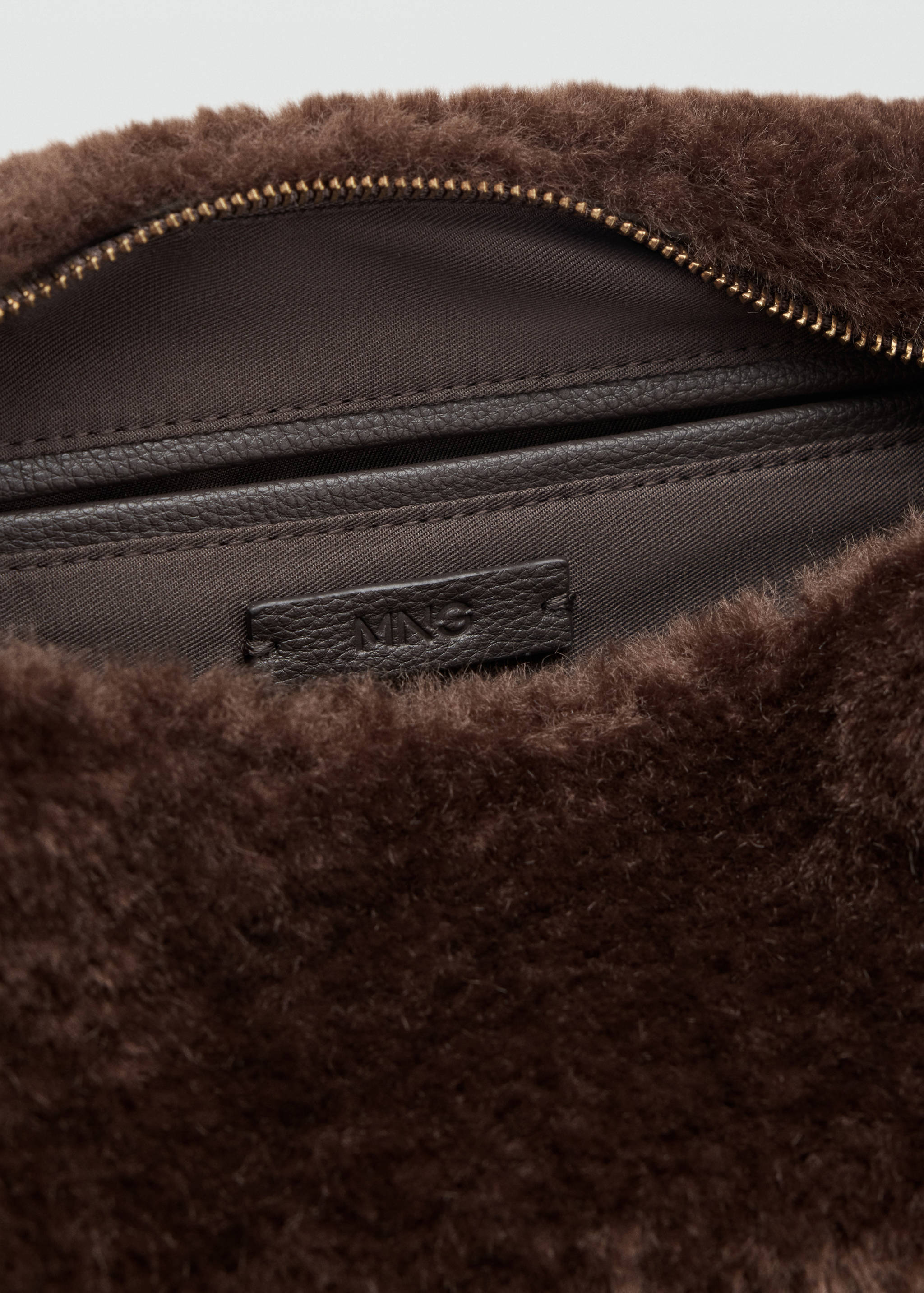 Close-up of the interior zip and lining of a dark brown faux-fur bag.
