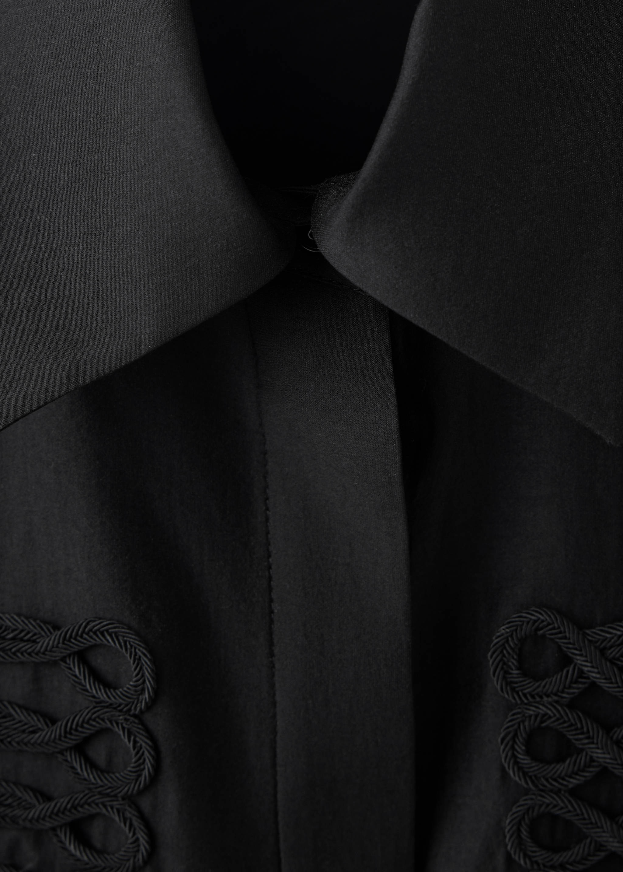 Close-up of a black shirt with a classic collar and tonal braided cord embroidery.