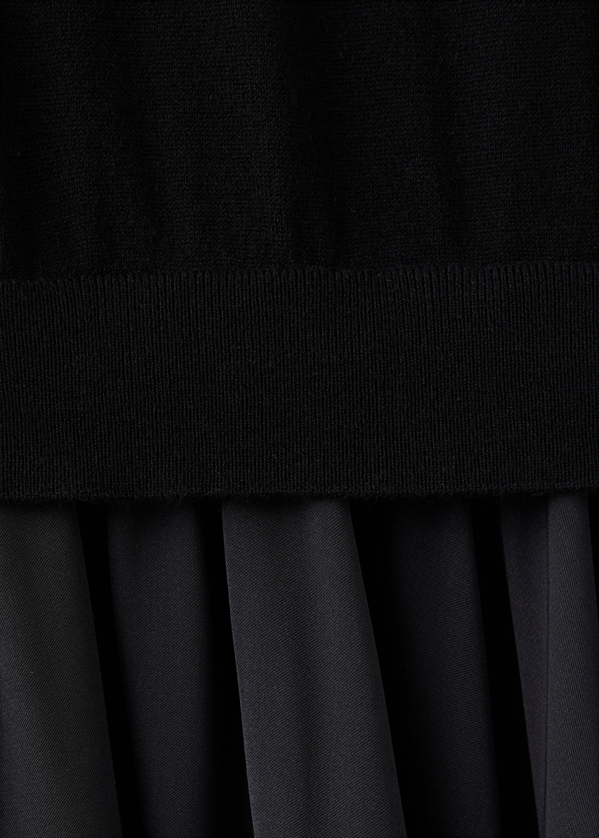 Black dress detail showing fine-knit bodice and pleated skirt