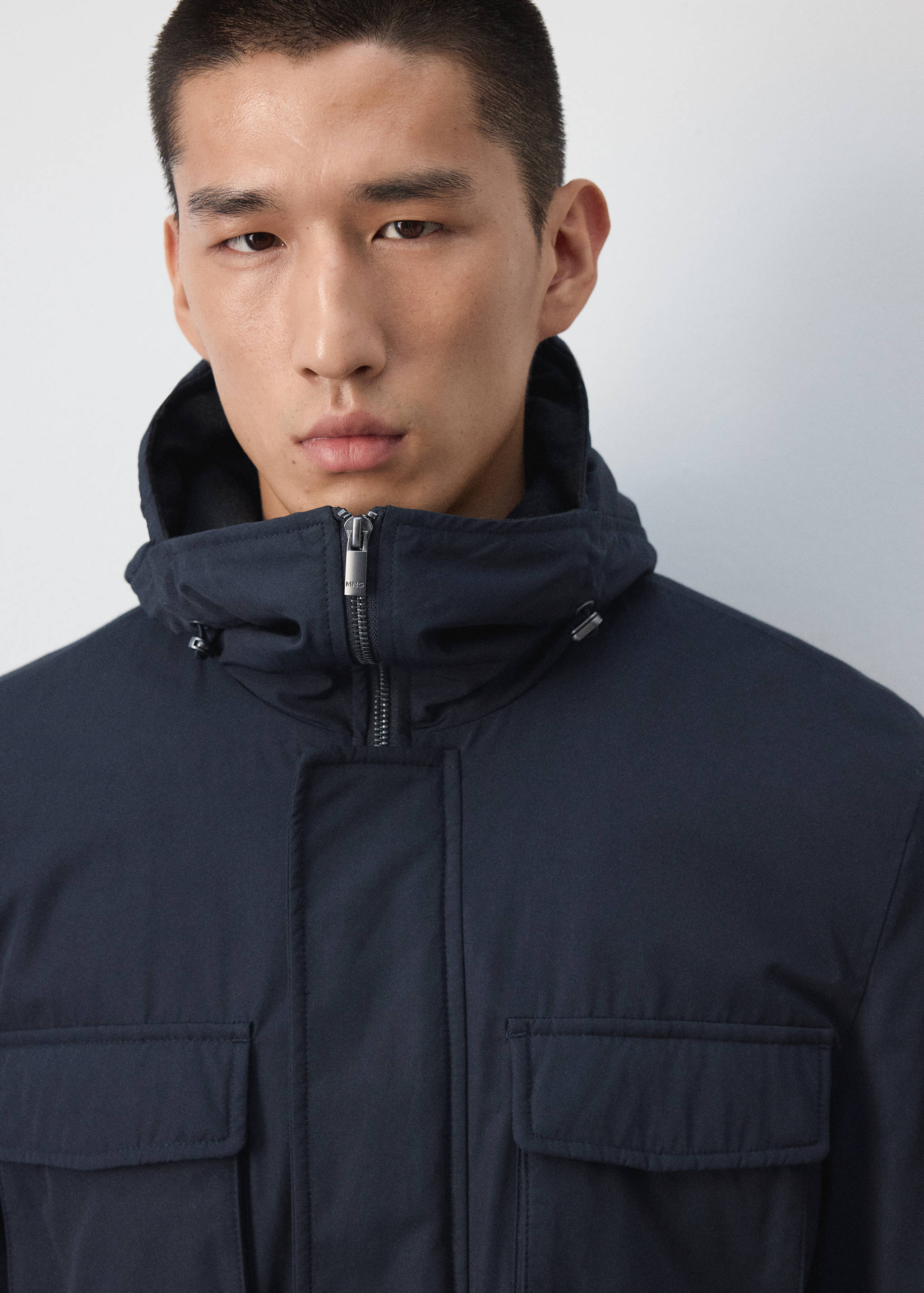 Close-up of a dark navy blue parka with a high collar, hood, and utility pockets.