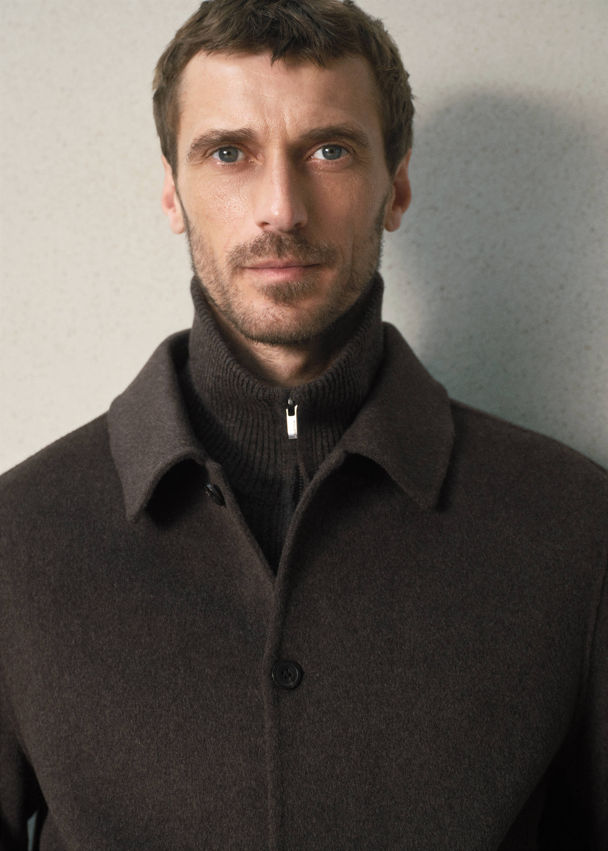 Dark brown jacket with a classic collar, worn over a ribbed zip-up top.