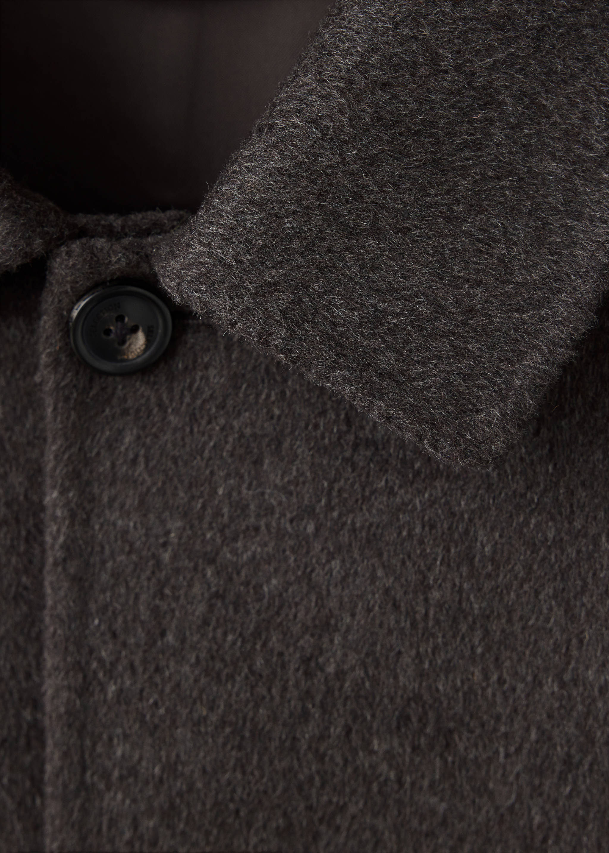 Close-up of a dark grey textured jacket collar and button.