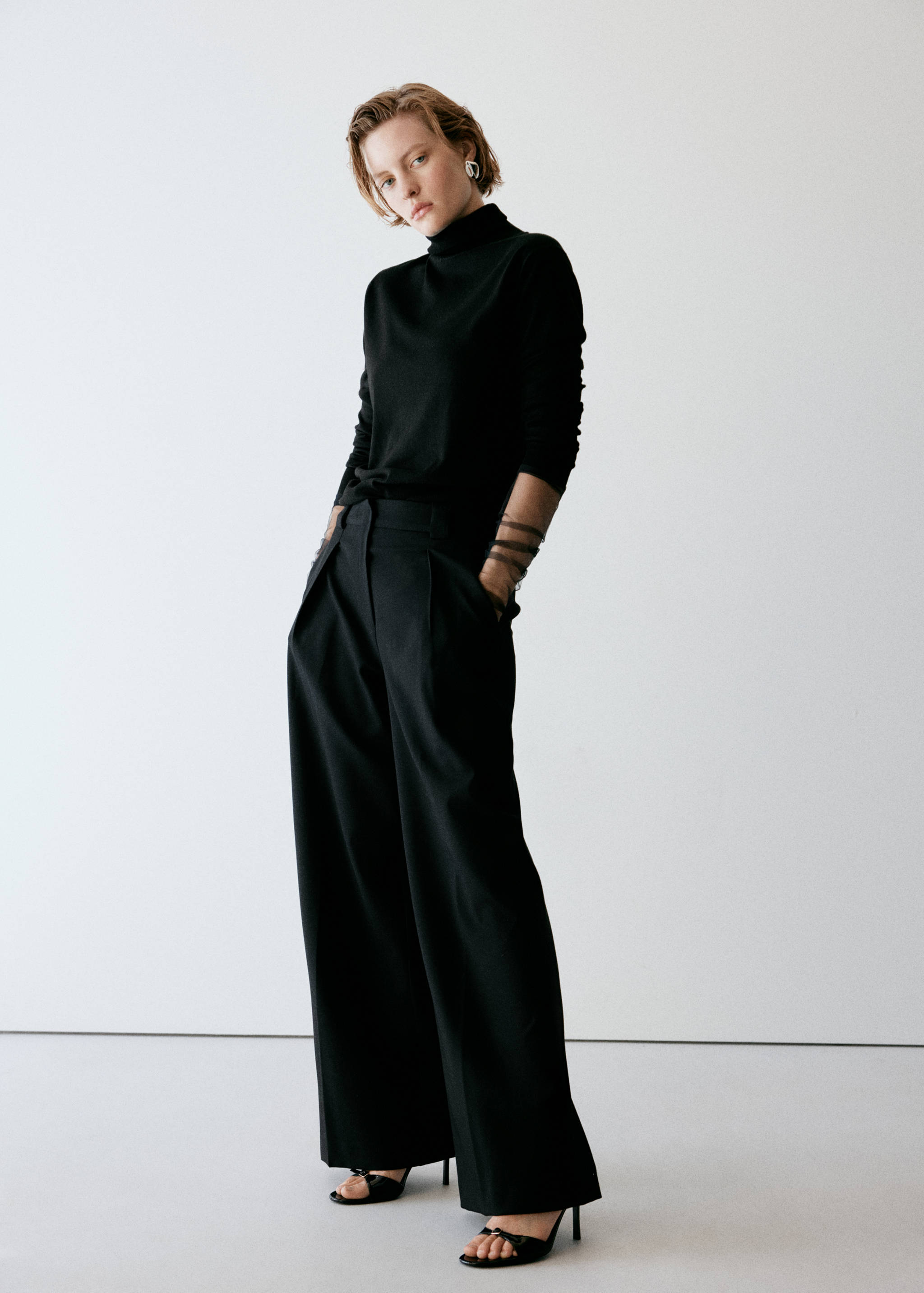 Black wide-leg trousers with front pleats, worn with a black turtleneck top.