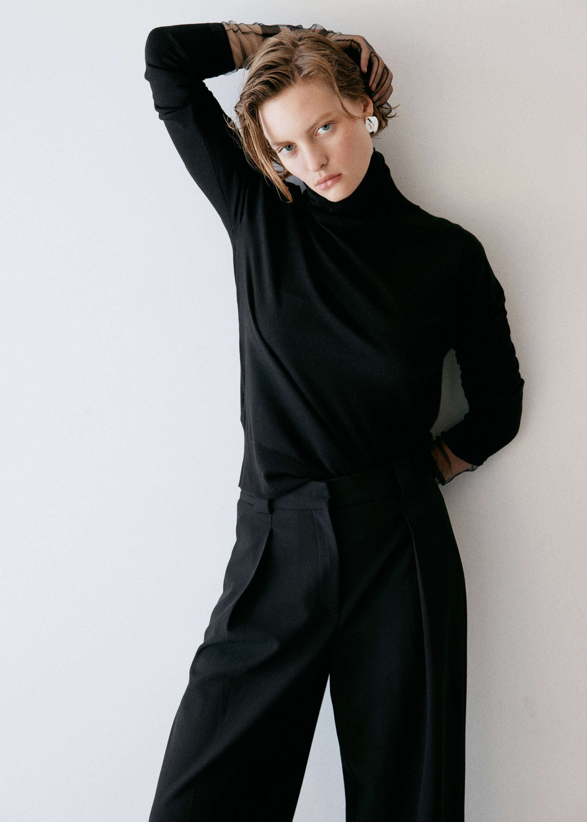 Black trousers with front pleats, worn with a black turtleneck top.