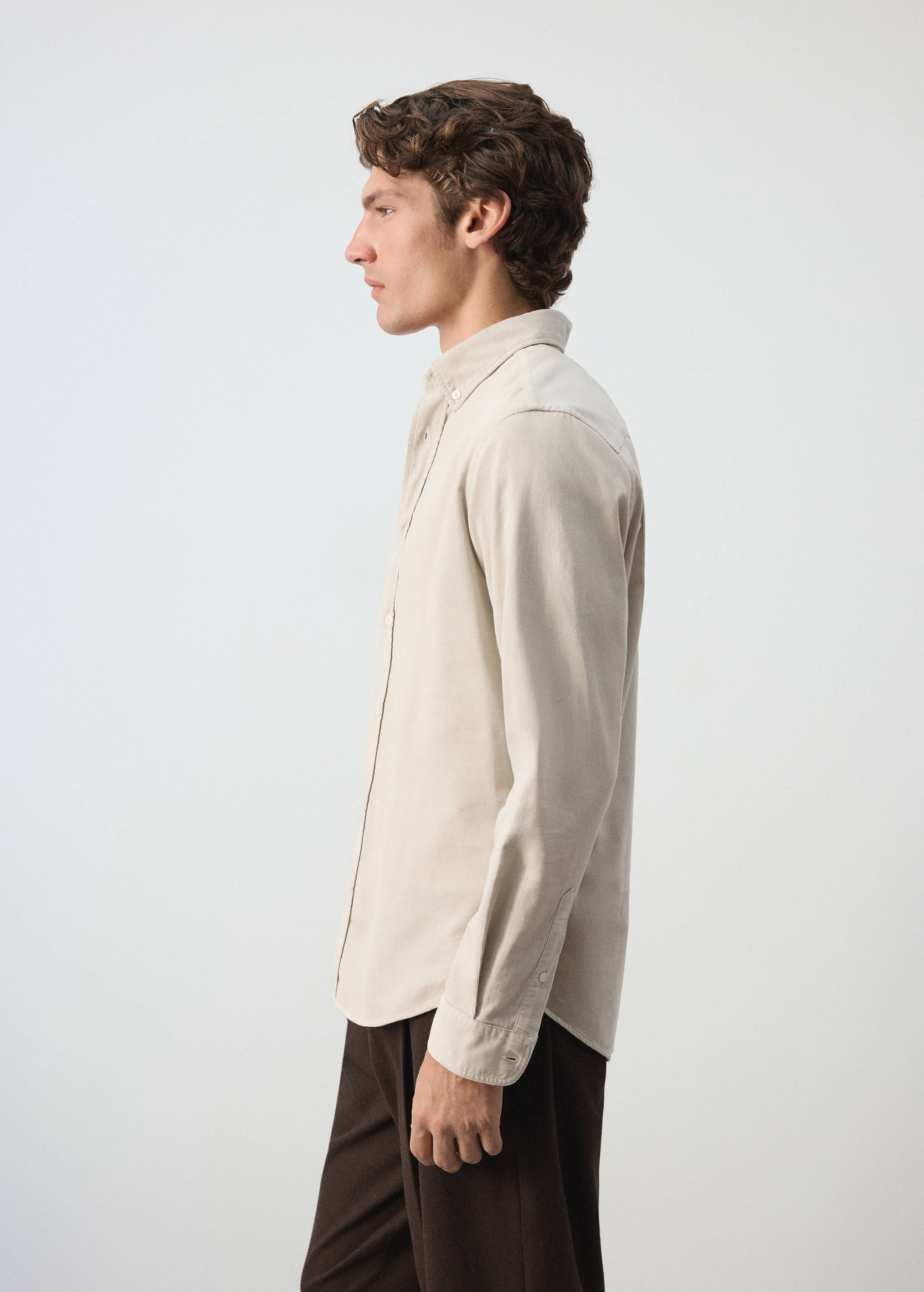 Beige long-sleeved button-down shirt worn with dark brown trousers.