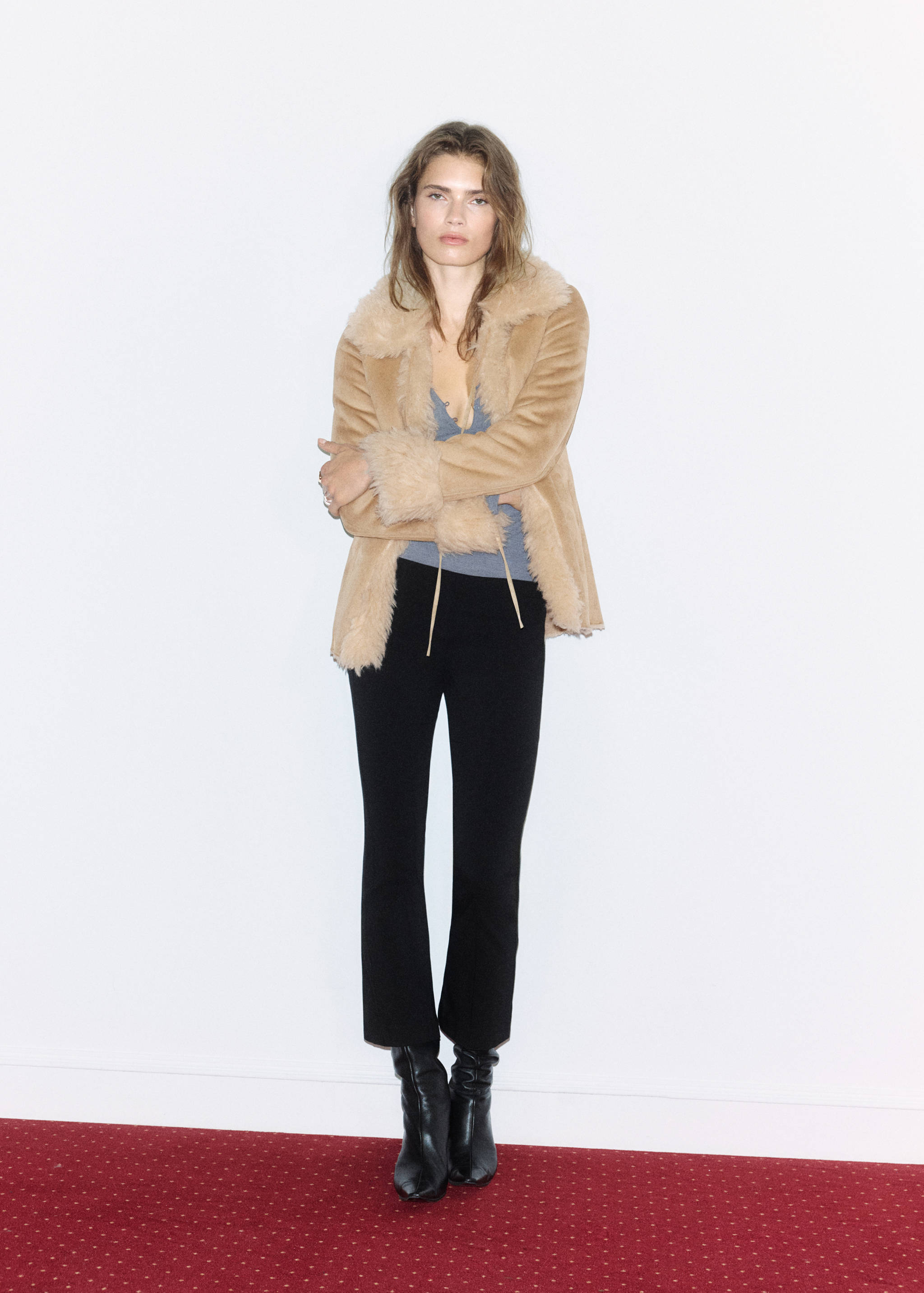 Camel faux-shearling jacket with wide lapels and fluffy trim, styled with a grey top and black trousers.