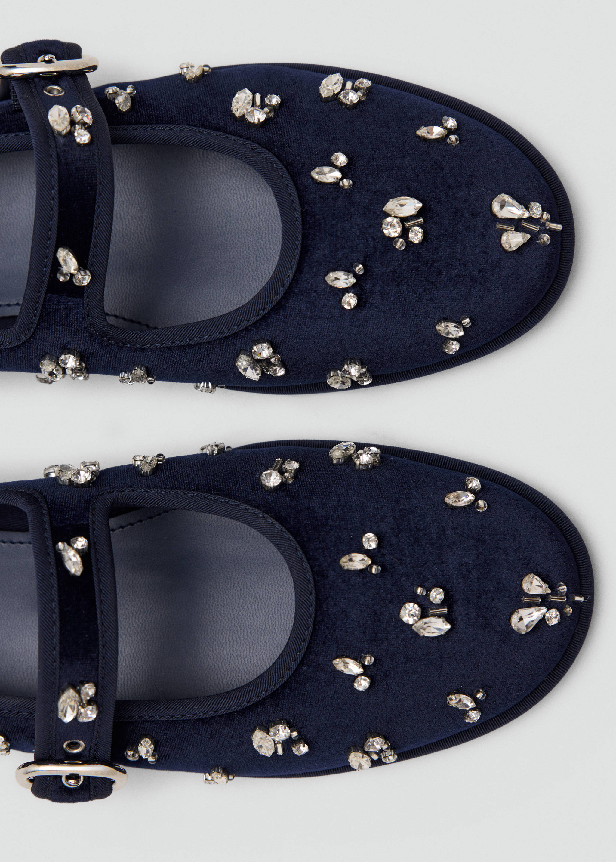 Close-up of navy blue velvet shoes with crystal embellishments and straps.