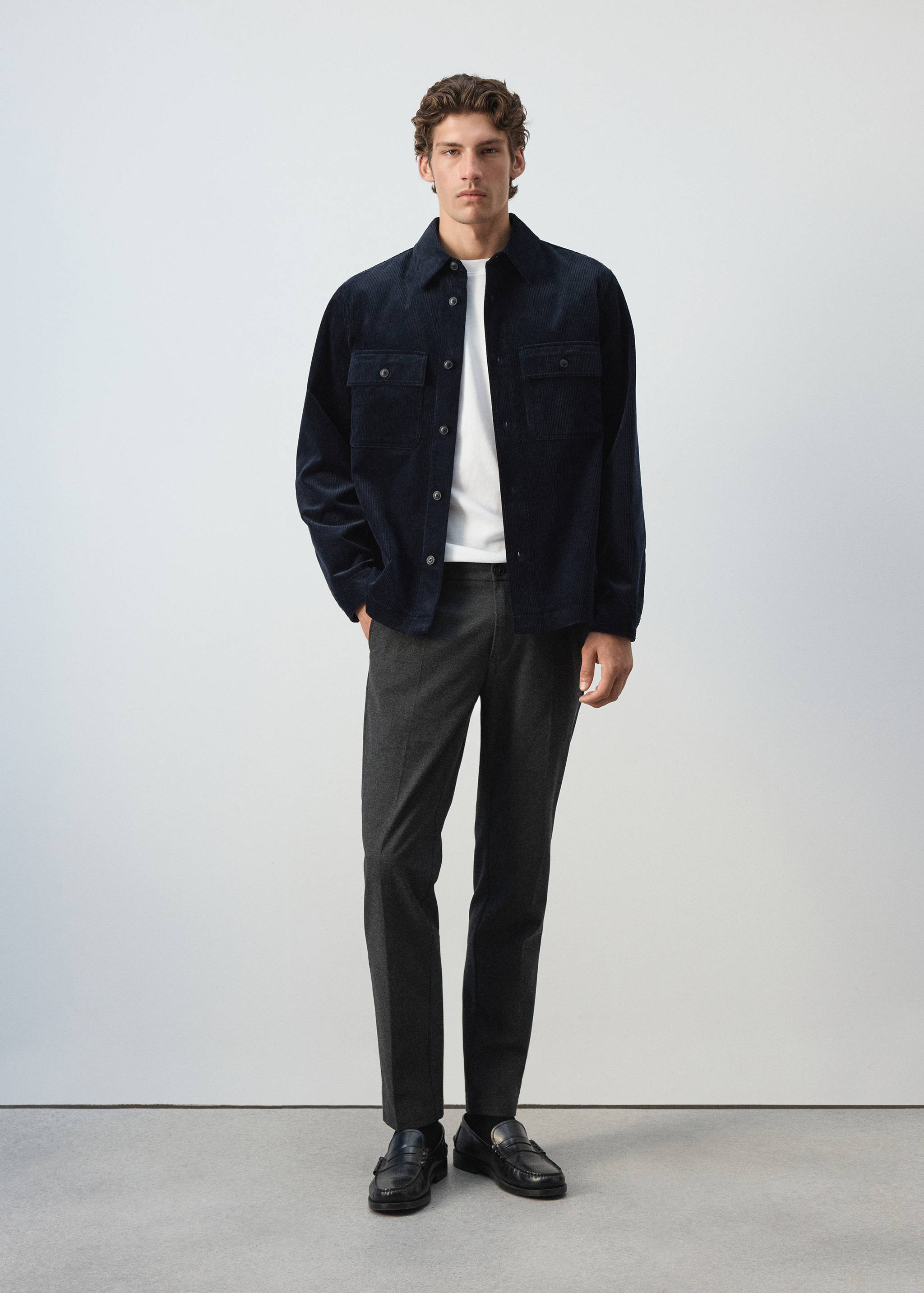 Navy blue corduroy overshirt worn with a white t-shirt and grey trousers.