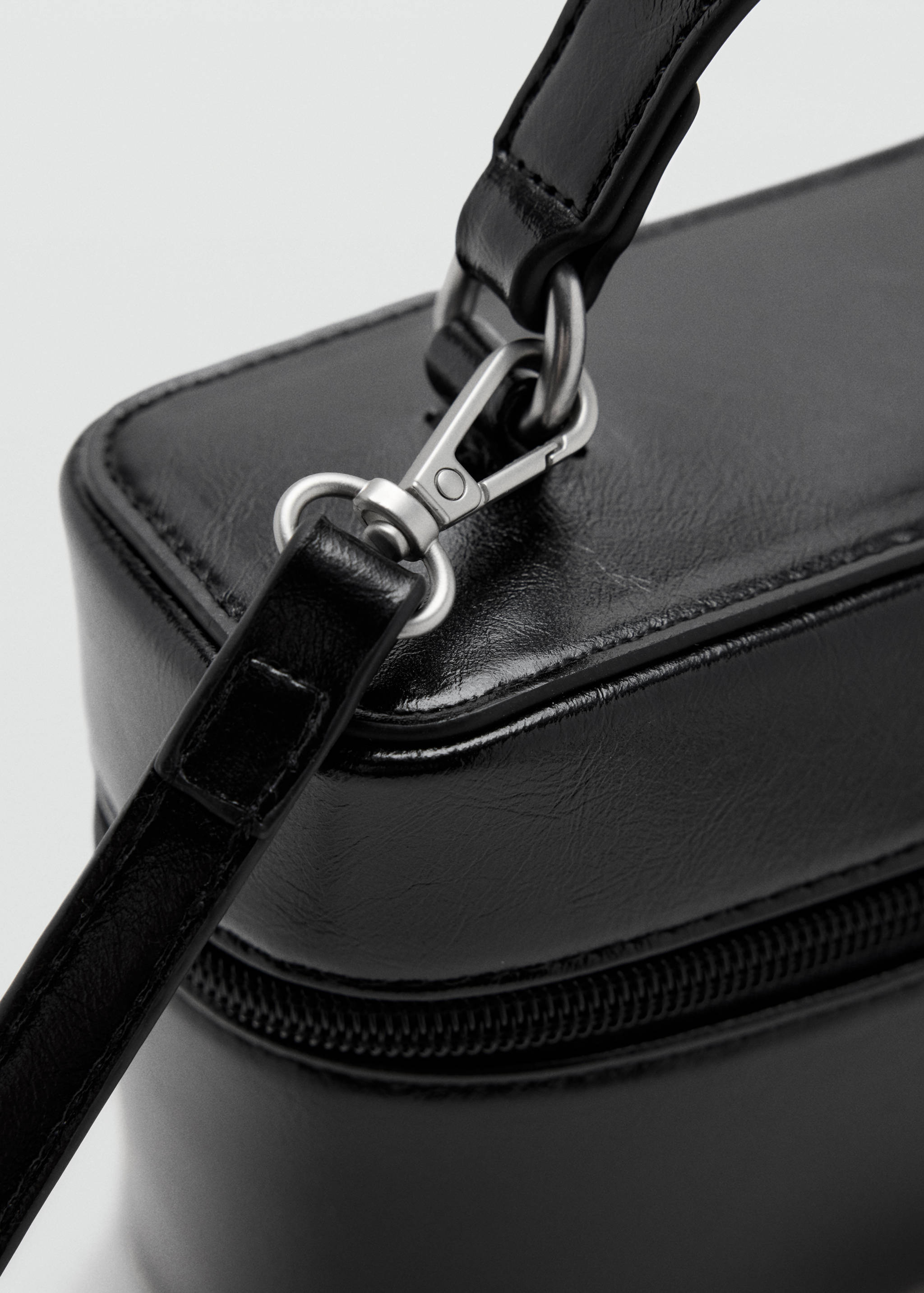 Close-up of a black mini bag showing the strap hardware and zipper detail.
