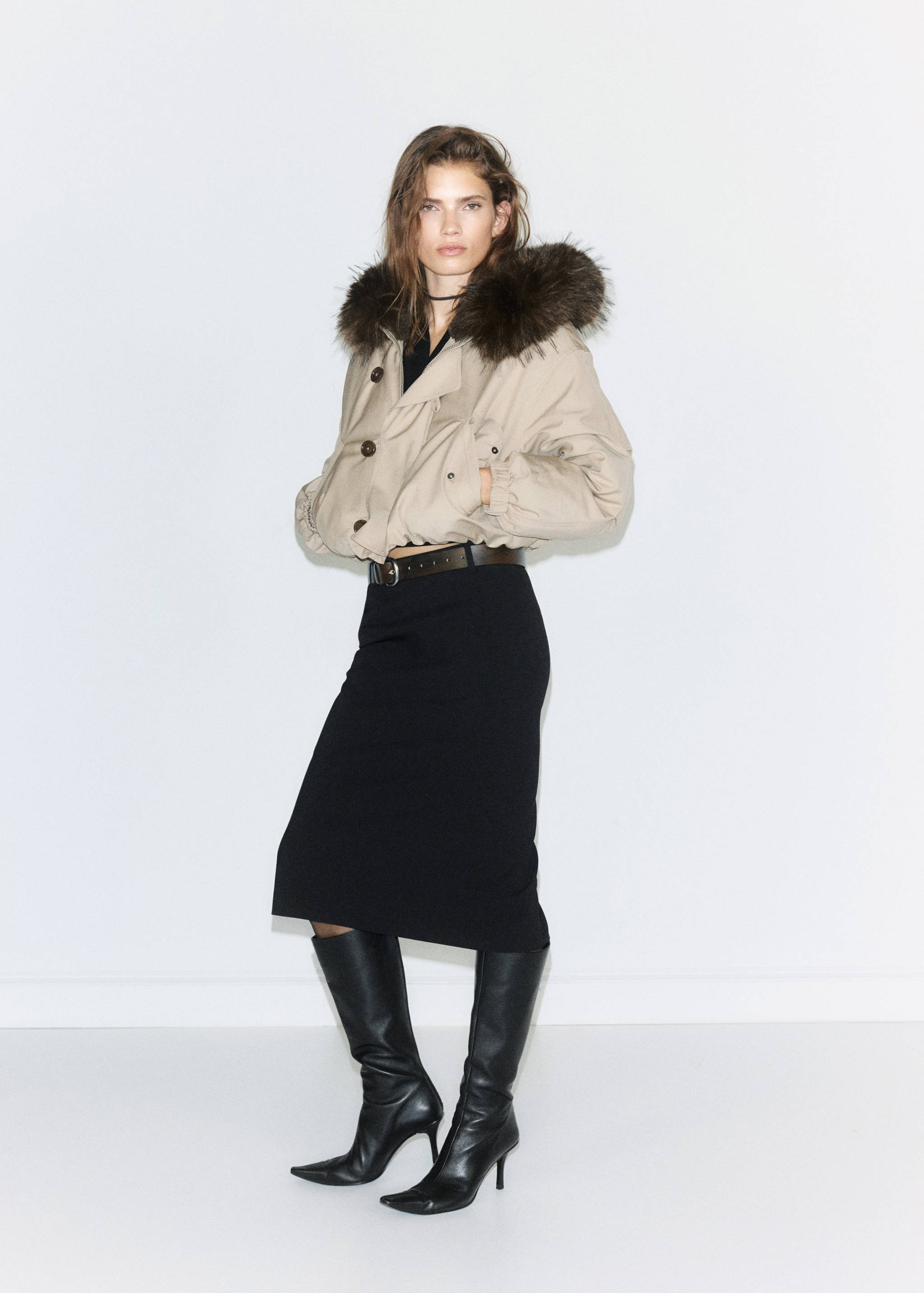 Beige cropped jacket with brown faux-fur trimmed hood, worn with a black midi skirt.