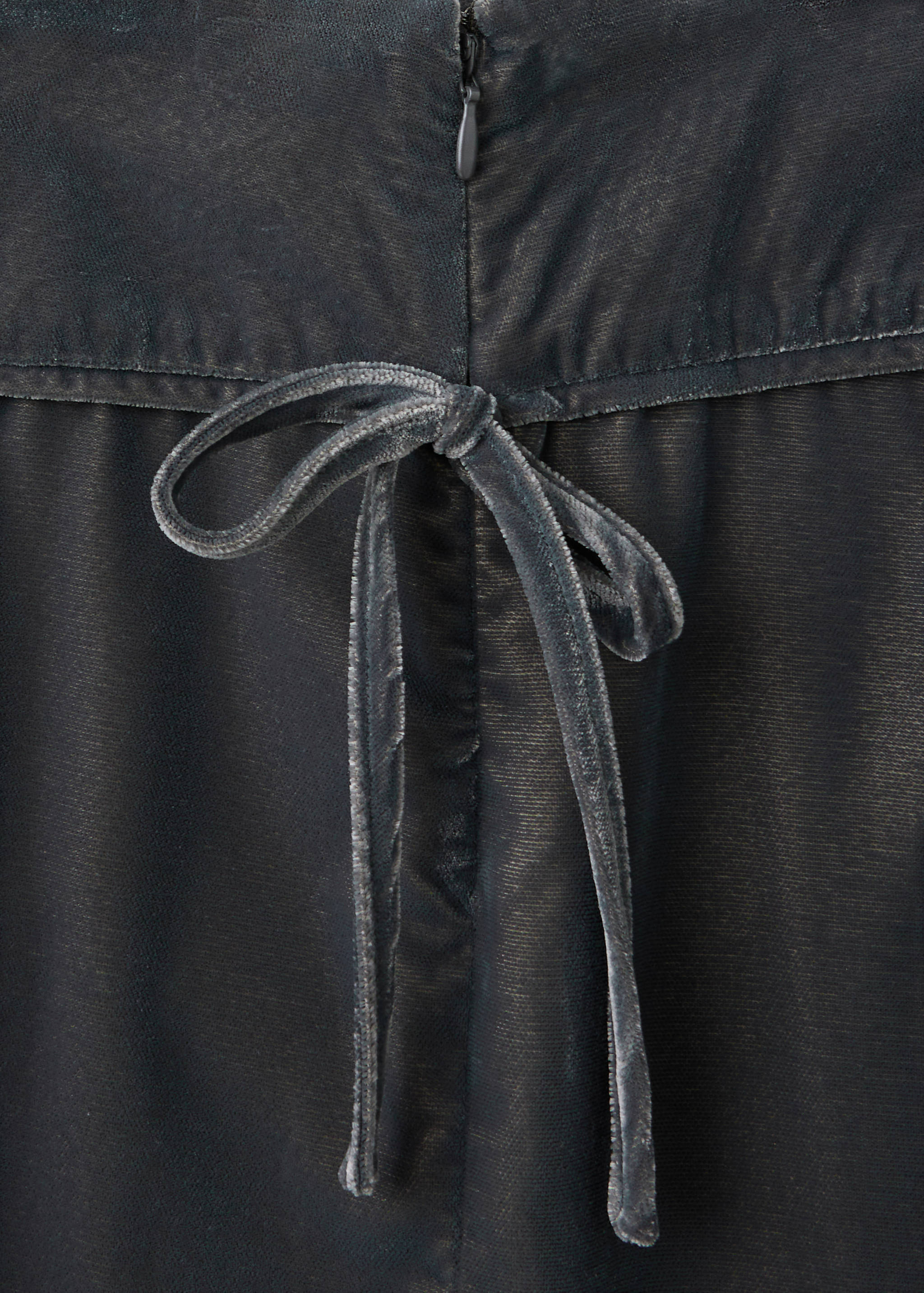 Close-up of grey trousers showing the waistband, zip, and velvet bow detail.