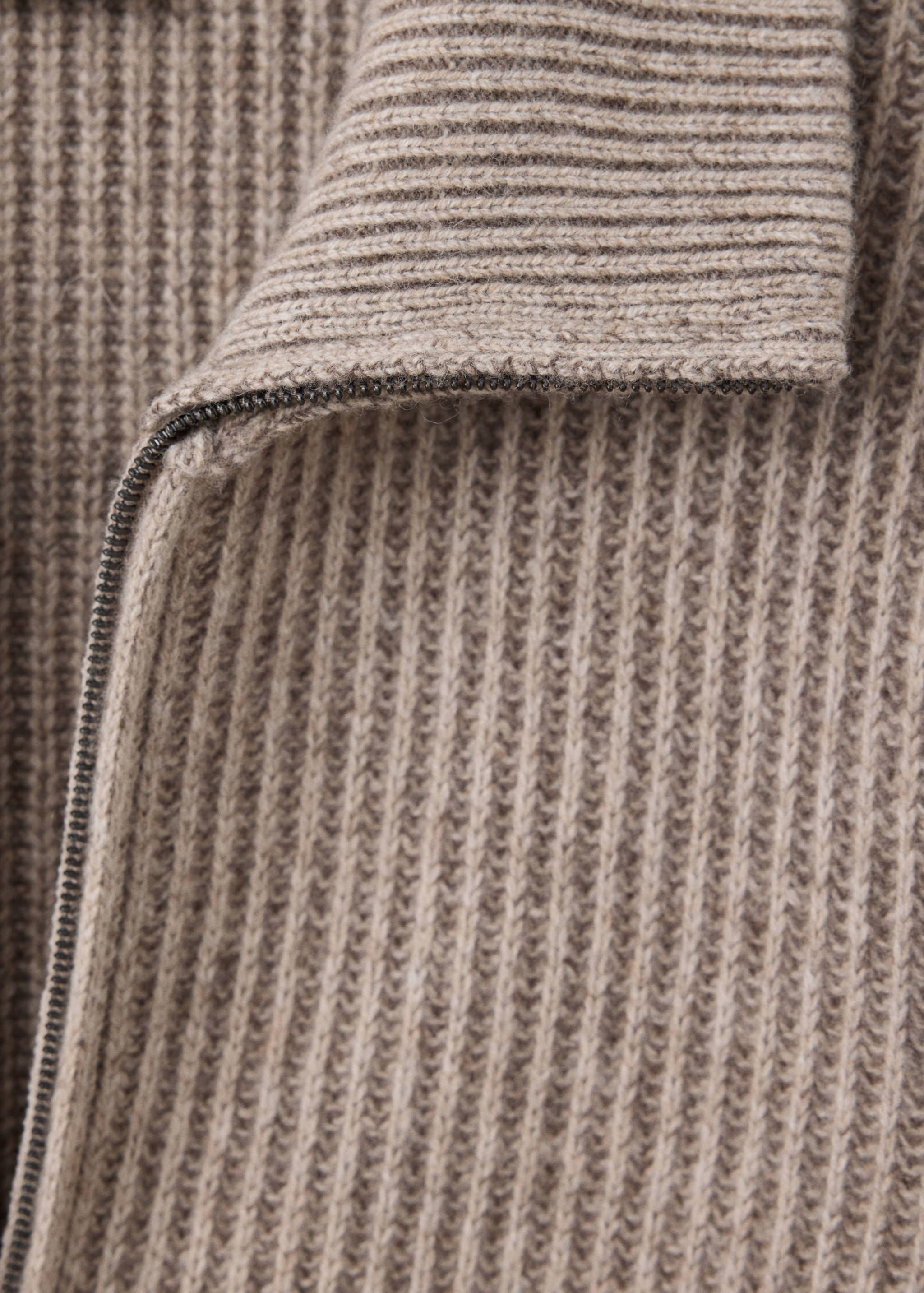 Close-up of a beige ribbed knit cardigan with a zip.