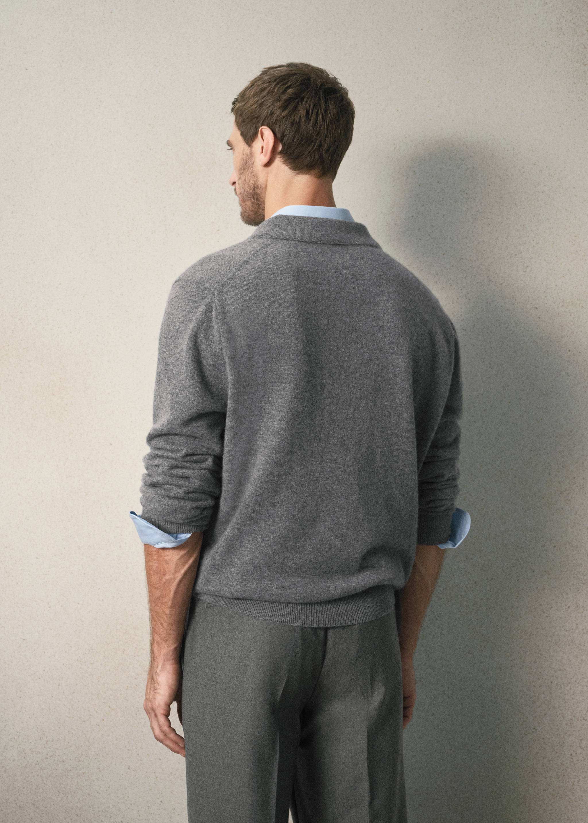Grey knitted polo seen from the back, layered over a light blue shirt.