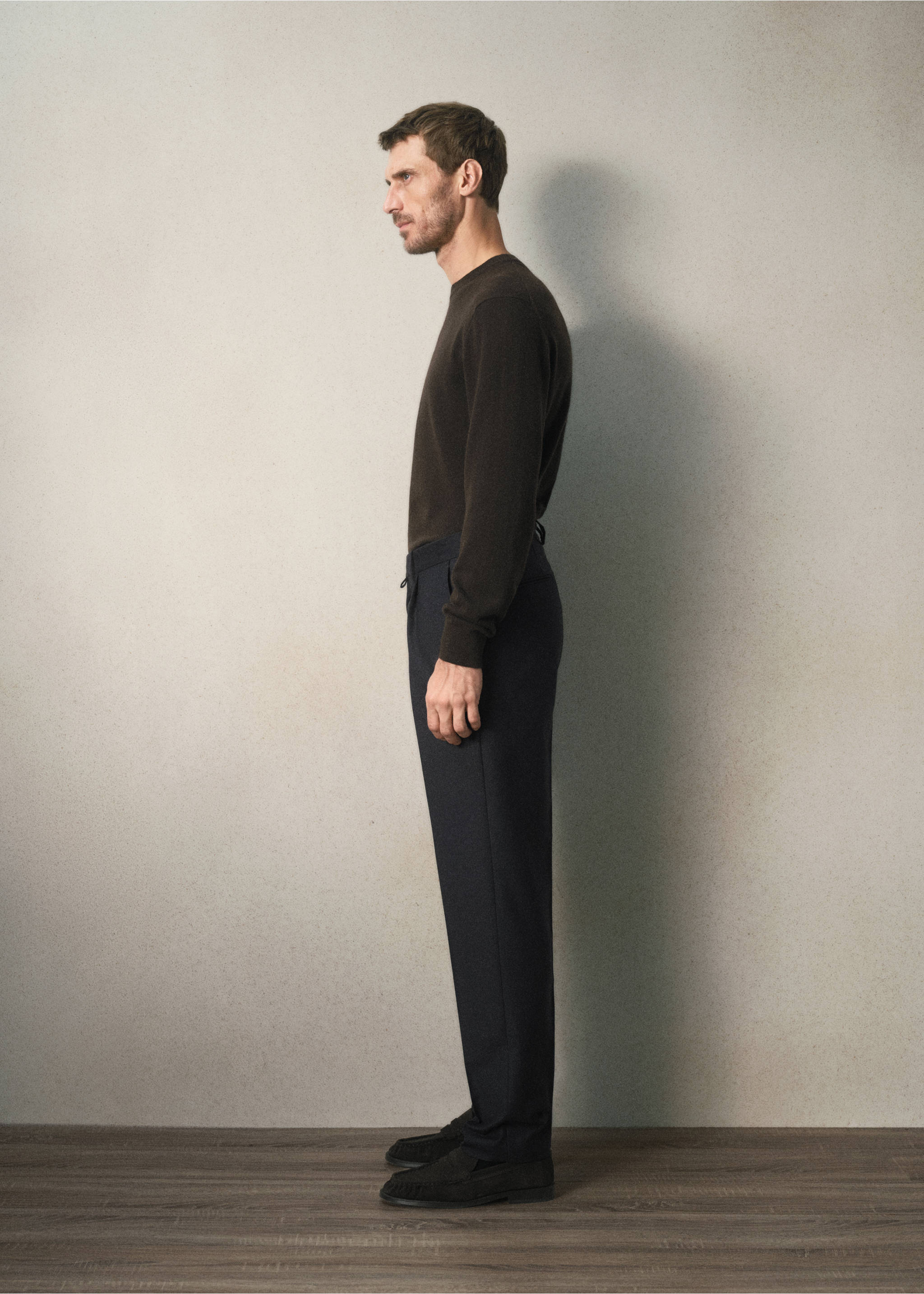 Dark trousers worn with a dark brown crew-neck sweater in profile view., Charcoal. Ref: 37088283-00.