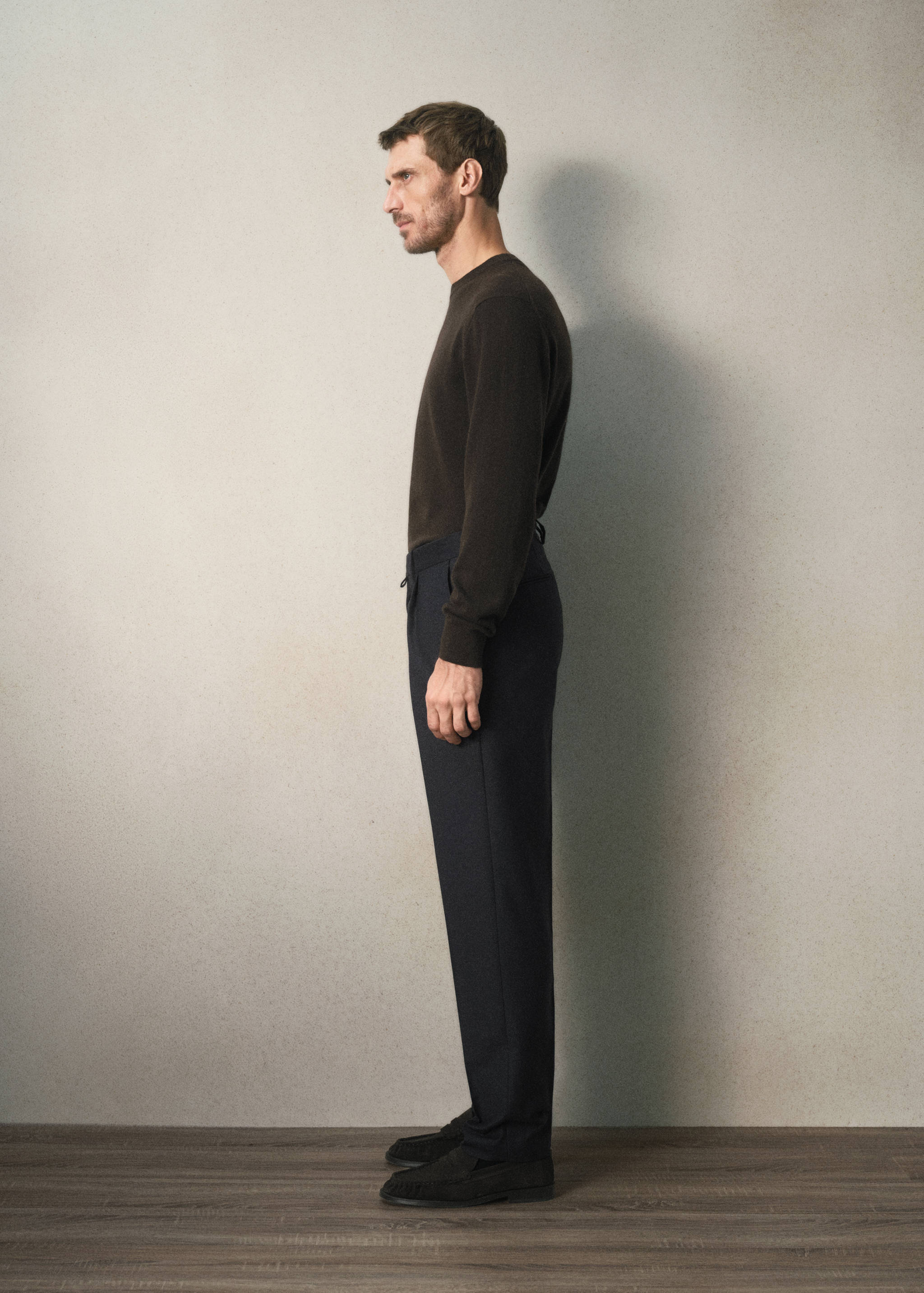 Dark trousers worn with a dark brown crew-neck sweater in profile view.